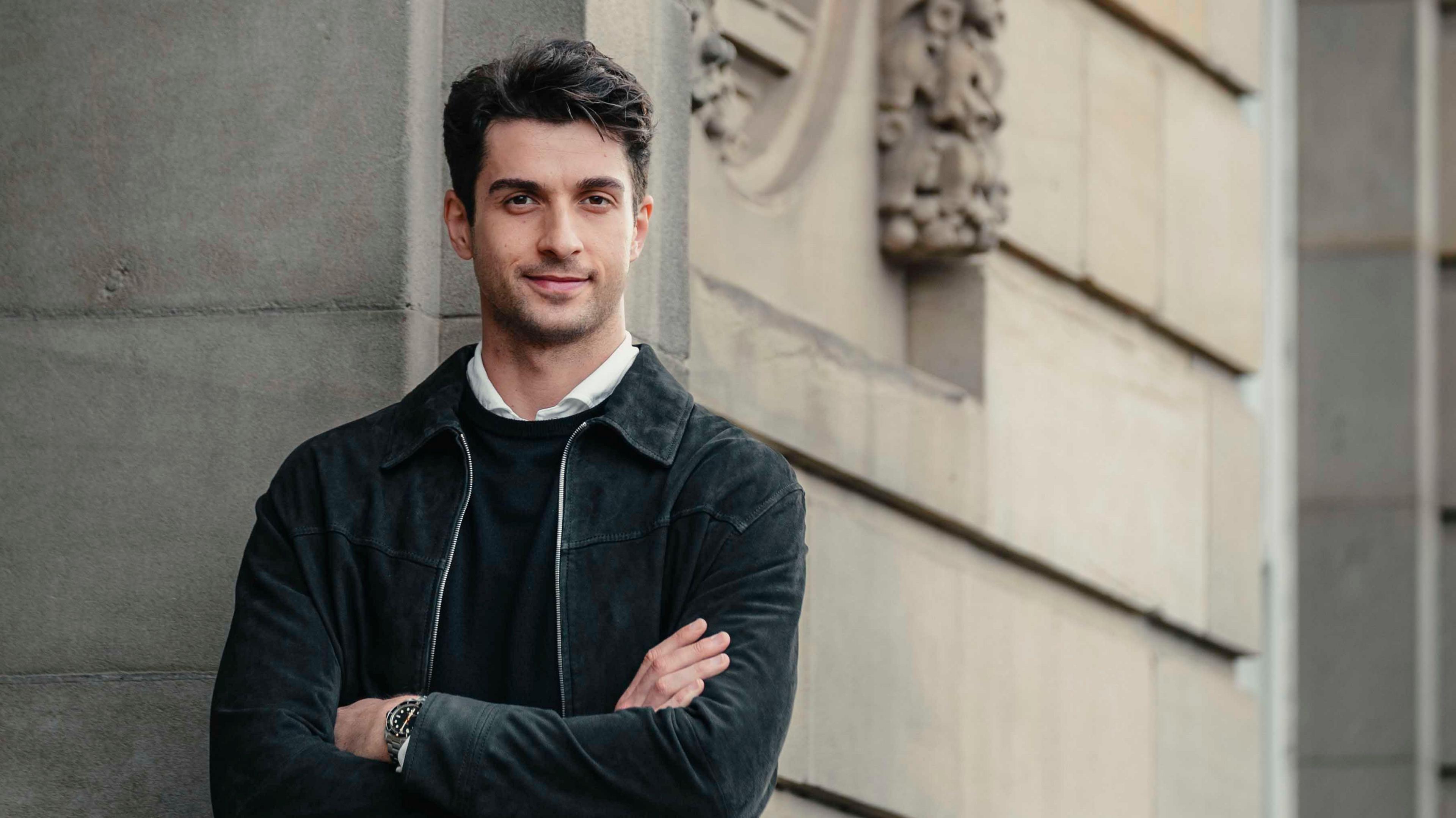 Reece Clarke with arms folded leans against sandstone brick wall