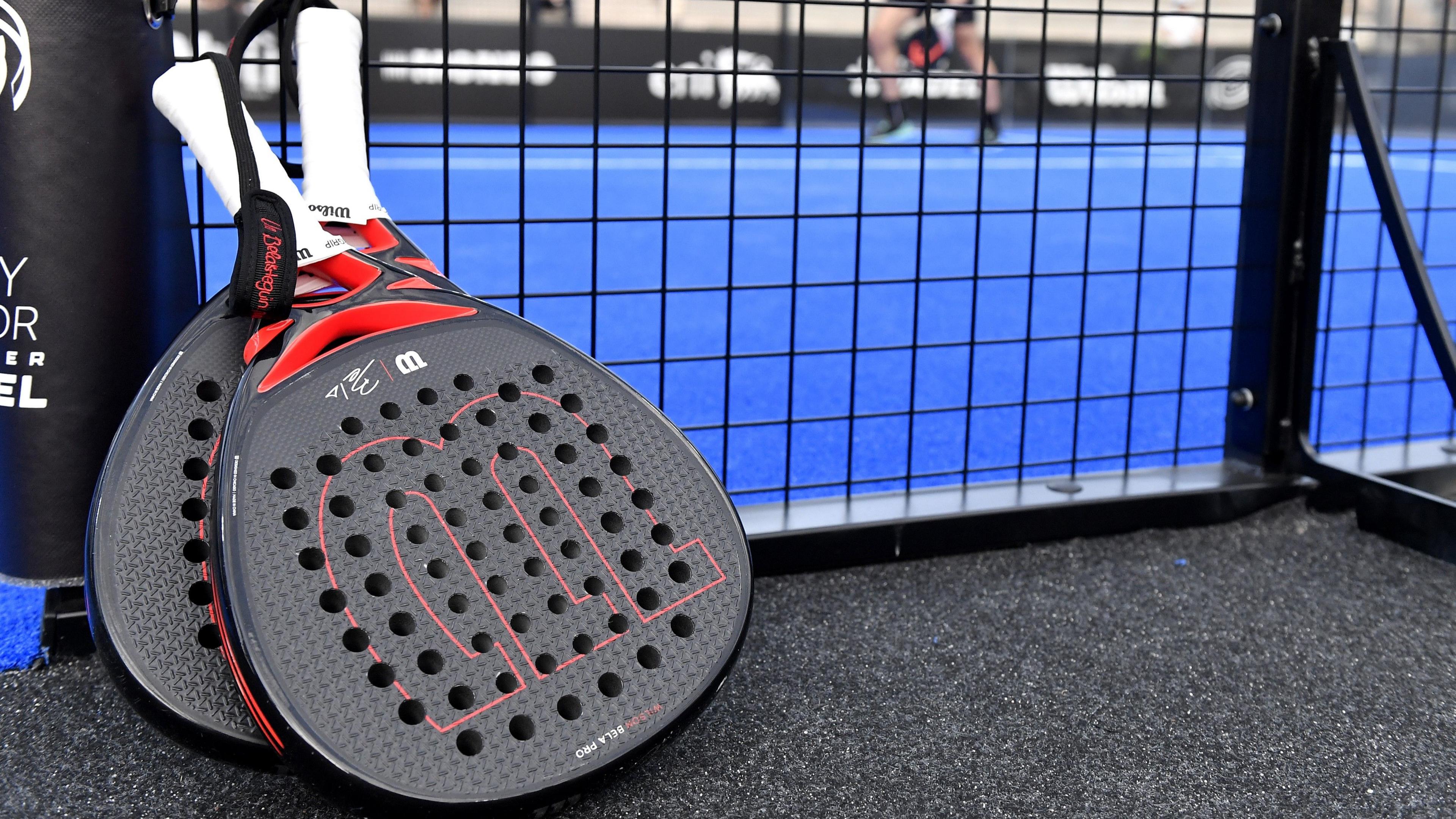 pair of padel rackets propped against a court netting - they are flatter and shorter than tennis rackets