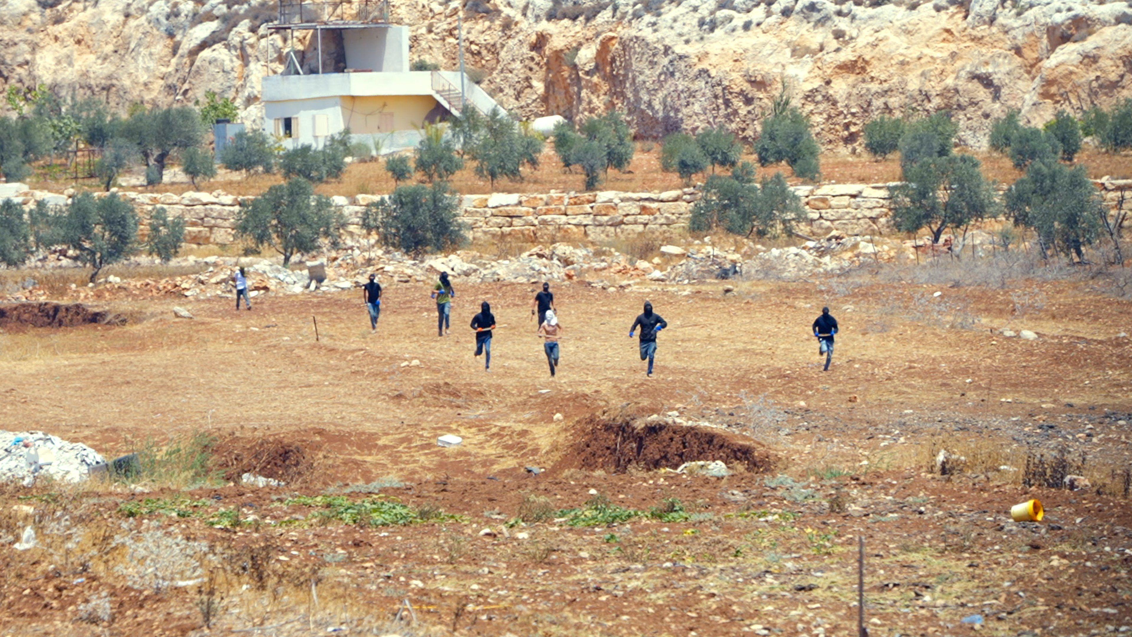 Several masked men run down a dry hill carrying various weapons
