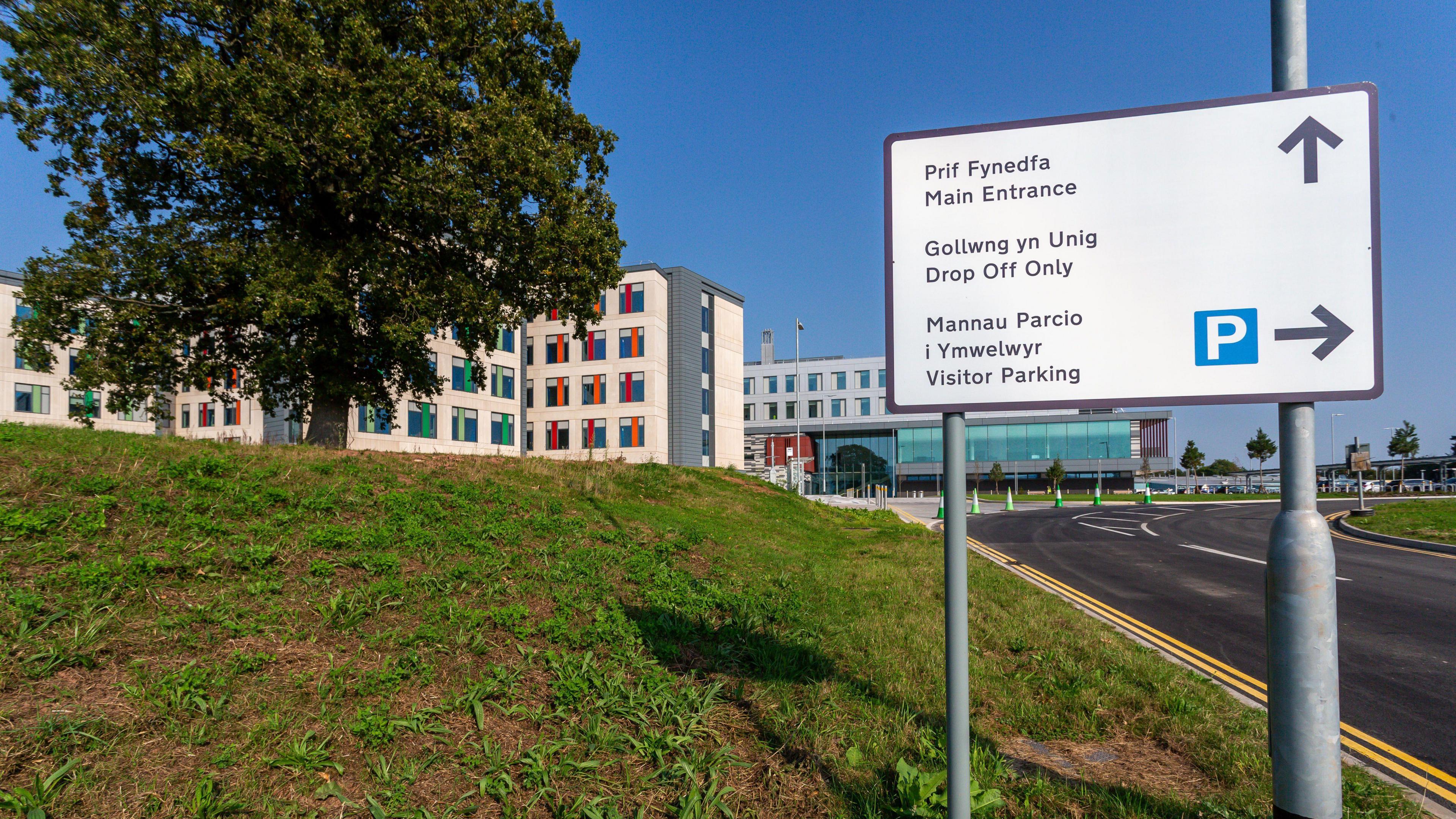 A general view to the signage as you enter The Grange University Hospital. Main entrance, Drop off only and visitor parking sign. In the background the hospital building is visible.
