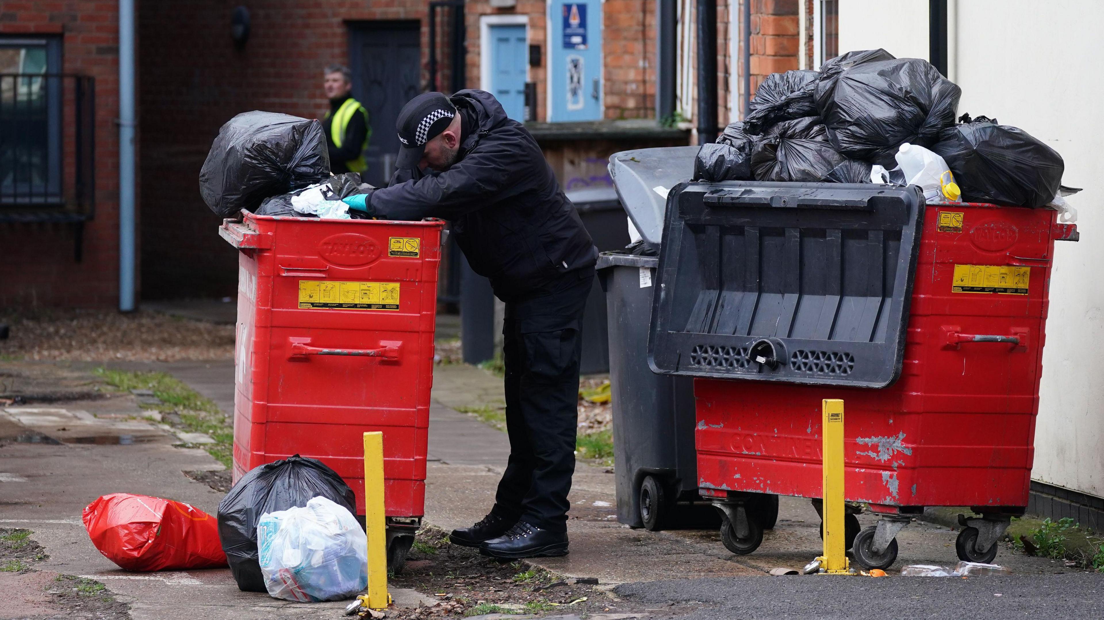 A police officer looking in a full to the brim Biffa bin