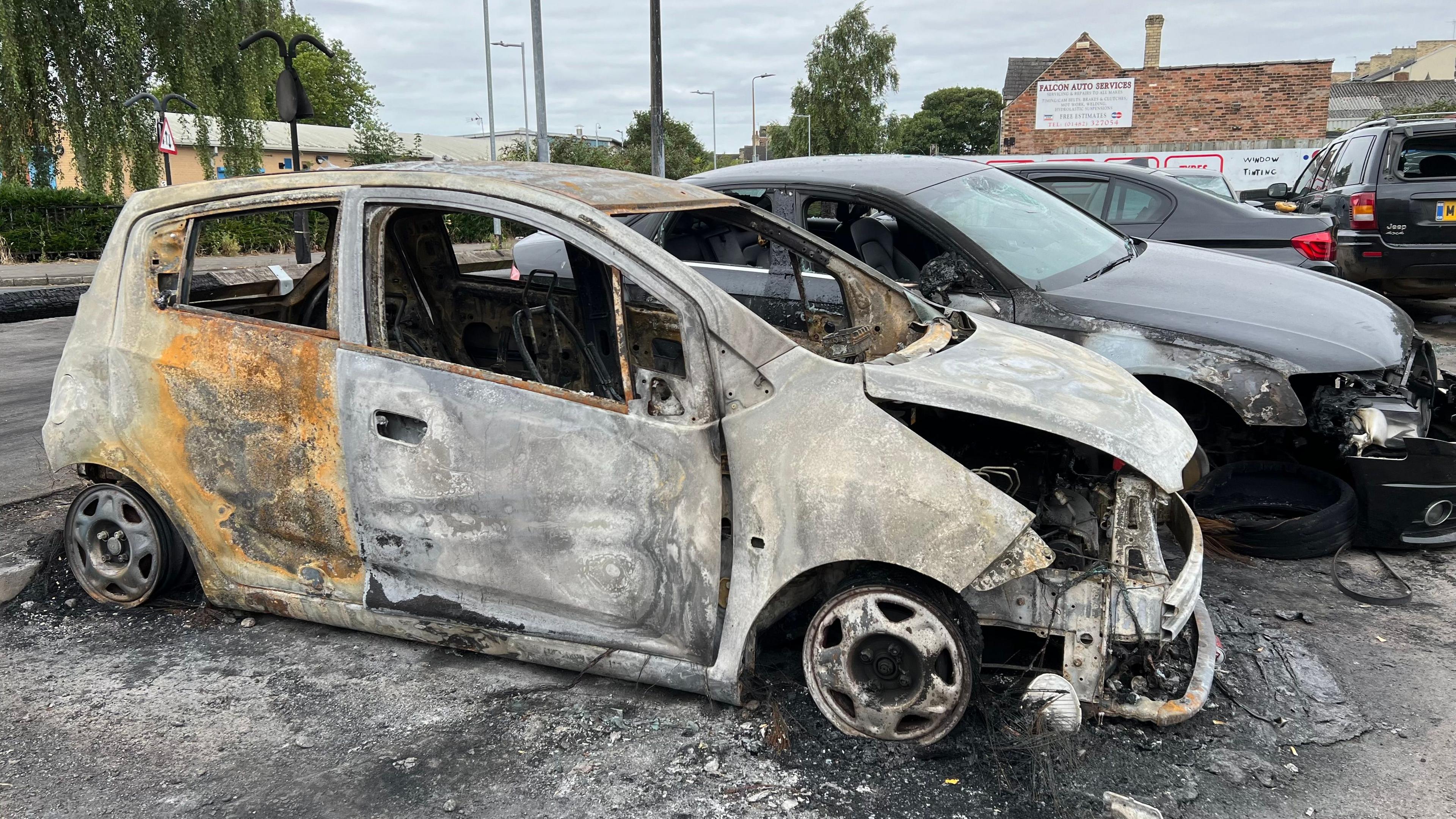 A car burnt out and damaged next to a line of other damaged cars