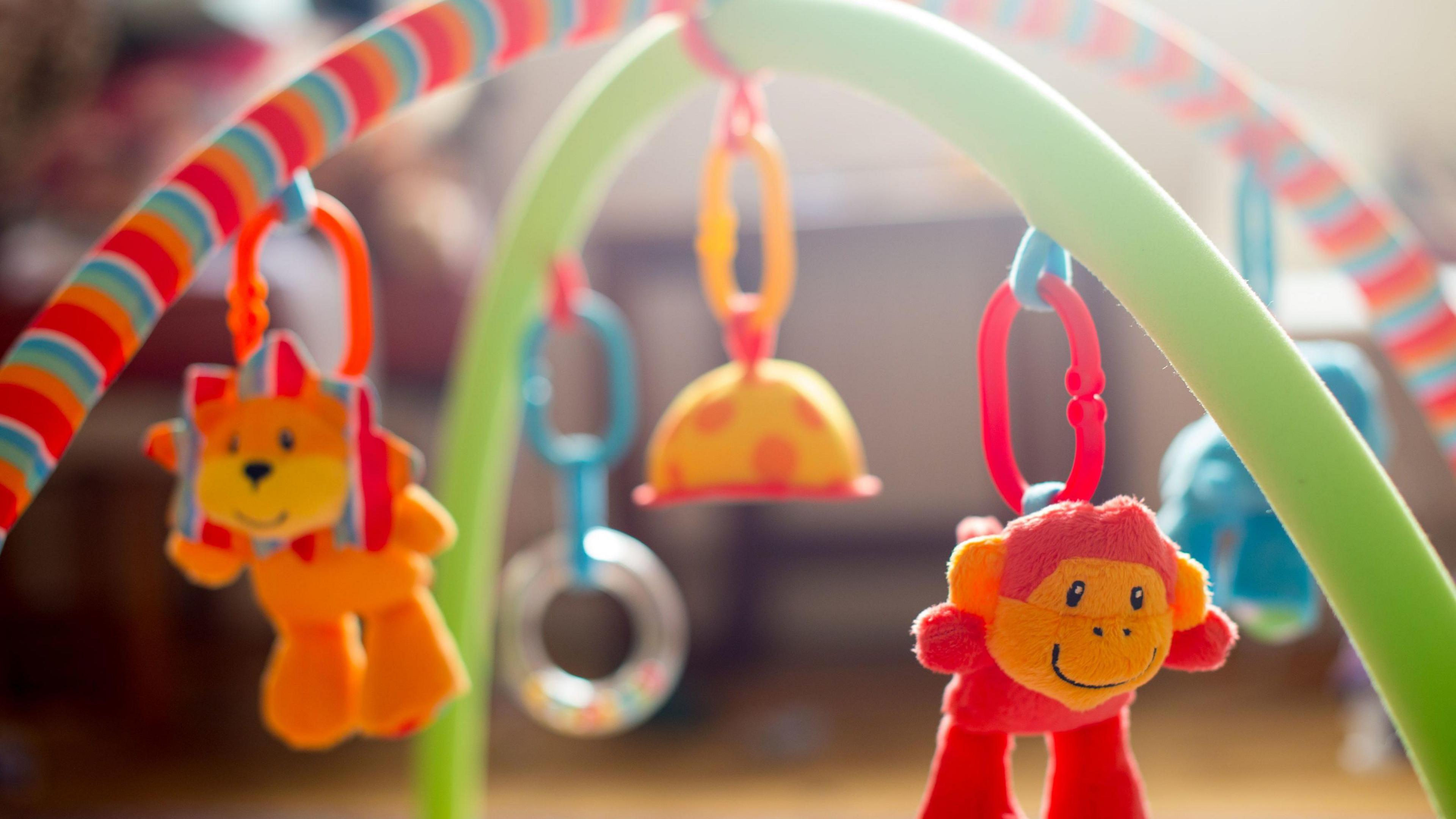 A baby mobile on an activity mat, there is a soft toy lion and monkey dangling from the frame.