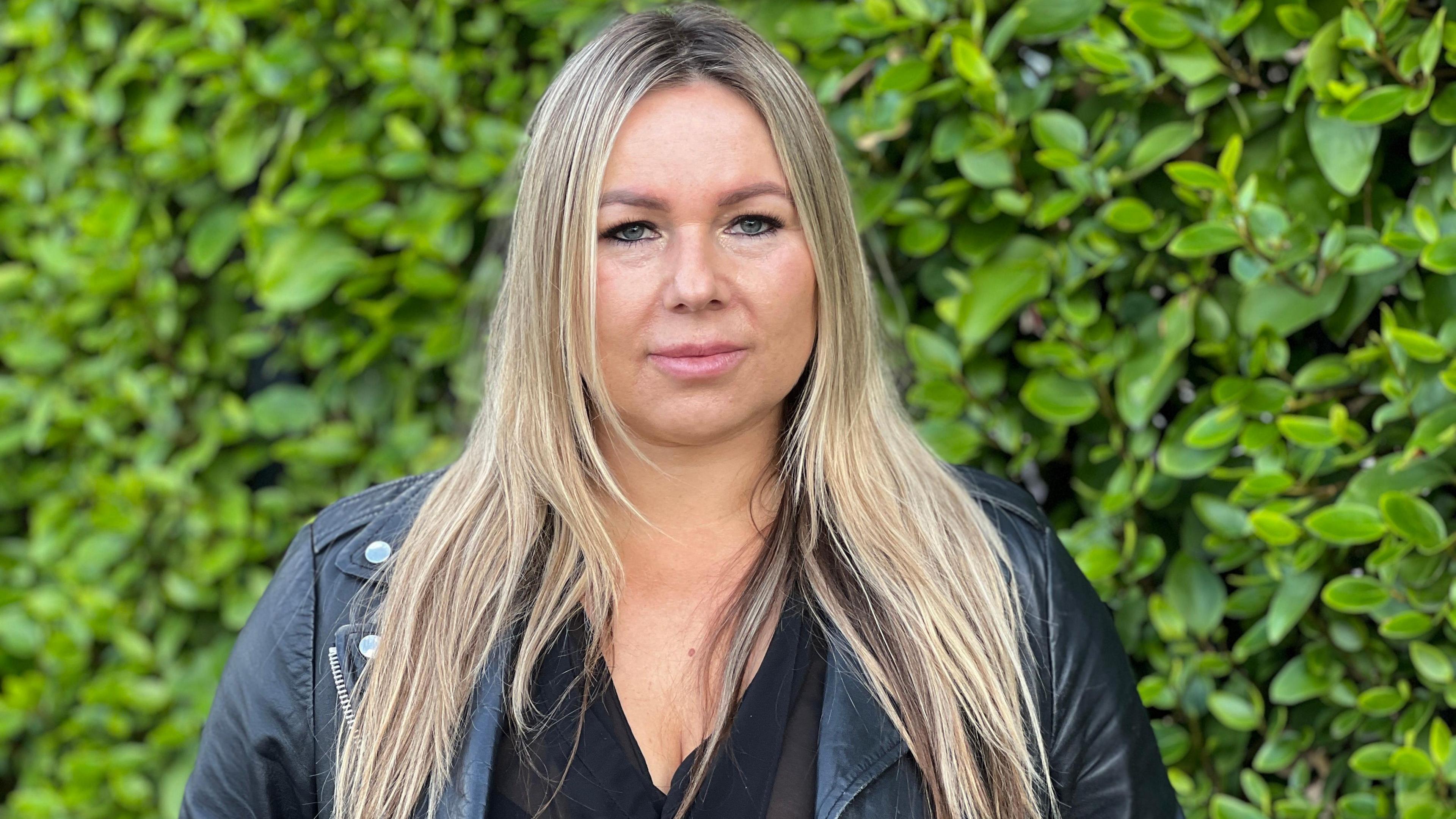 Anna Wasilewska has long blonde hair and is wearing a black leather jacket, as she looks directly at the camera.