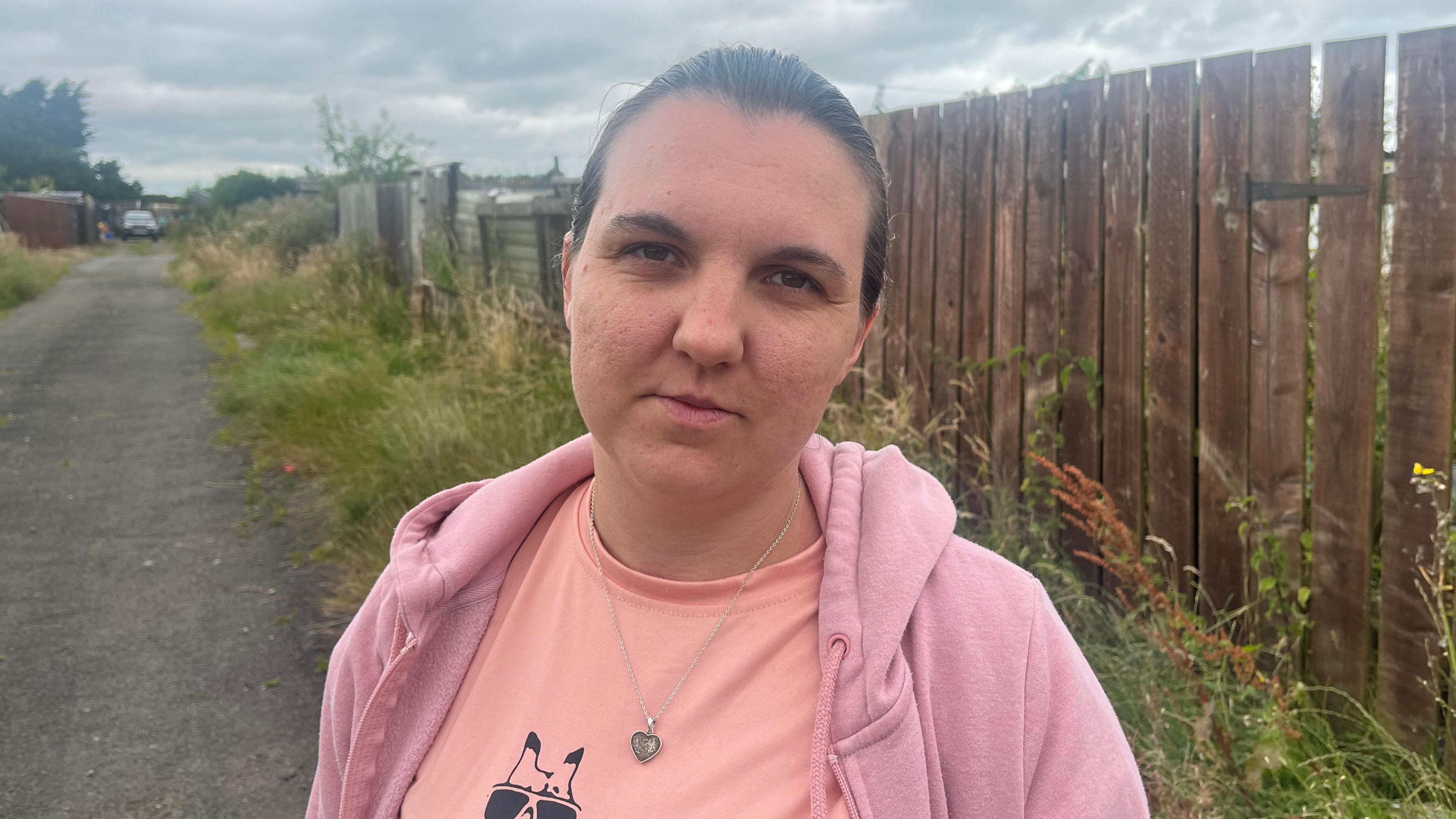 A woman in a pink hoody standing on a pathway next to allotments