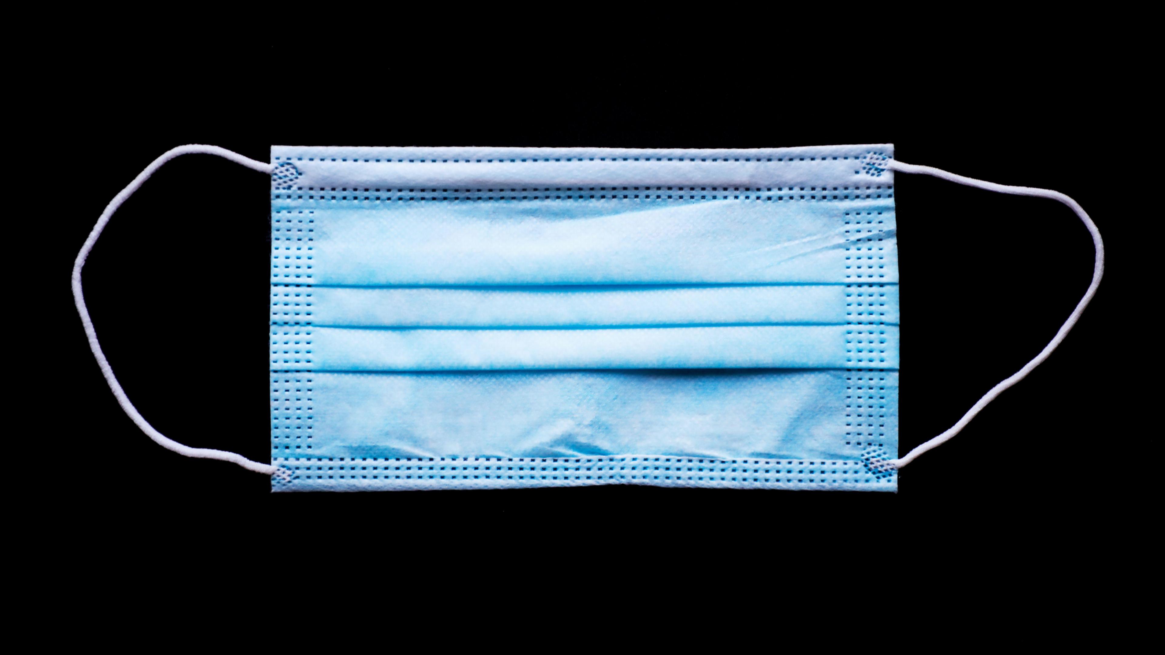 A close-up of a blue standard face-mask against a black background.