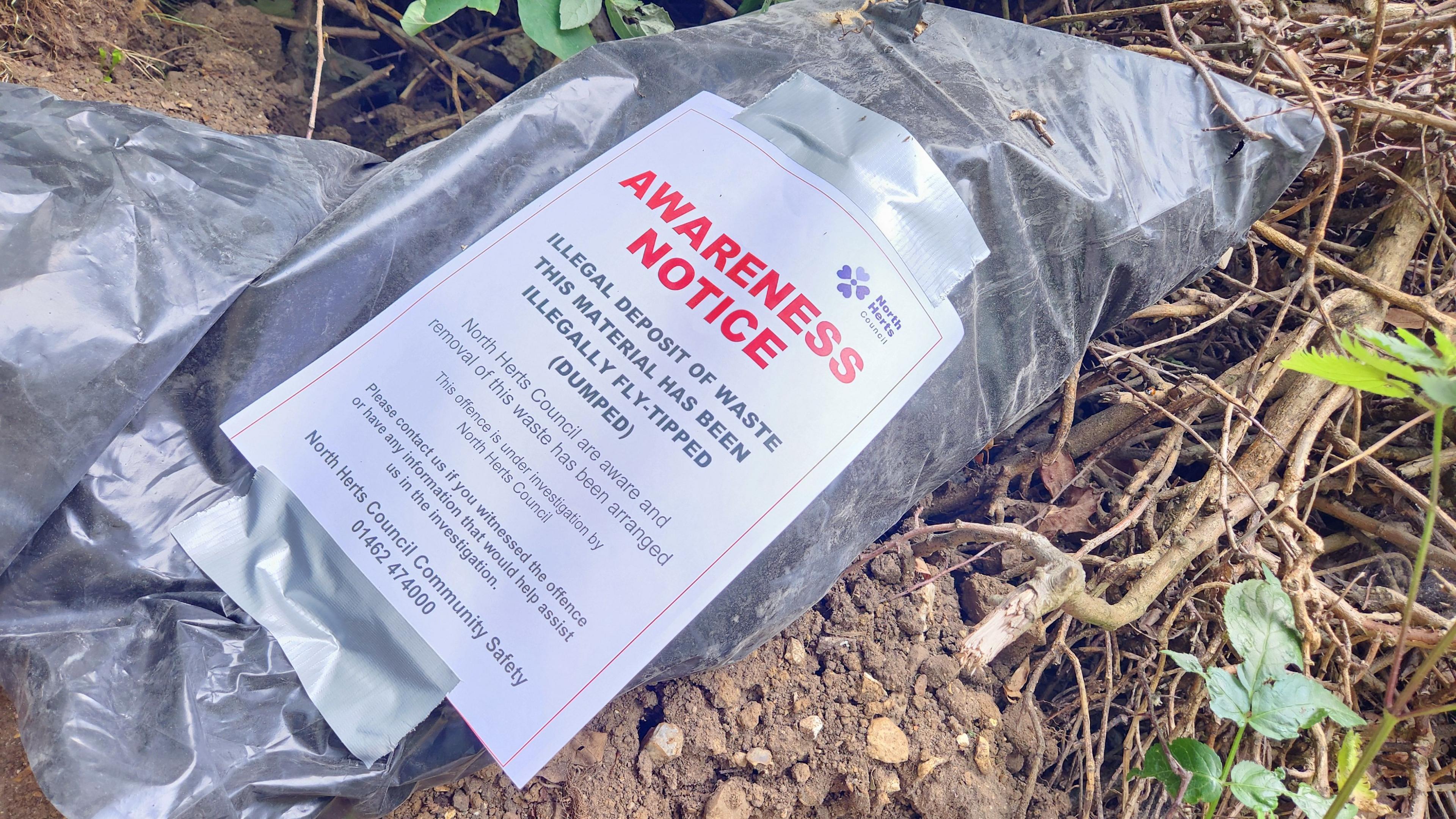 Dumped waste with a large notice on it from North Herts Council which reads in bold red font: "Awareness Notice". It goes on to say "illegal deposit of waste" and "this material has been illegally fly-tipped (dumped)". There then follows details of how you can contact the council.