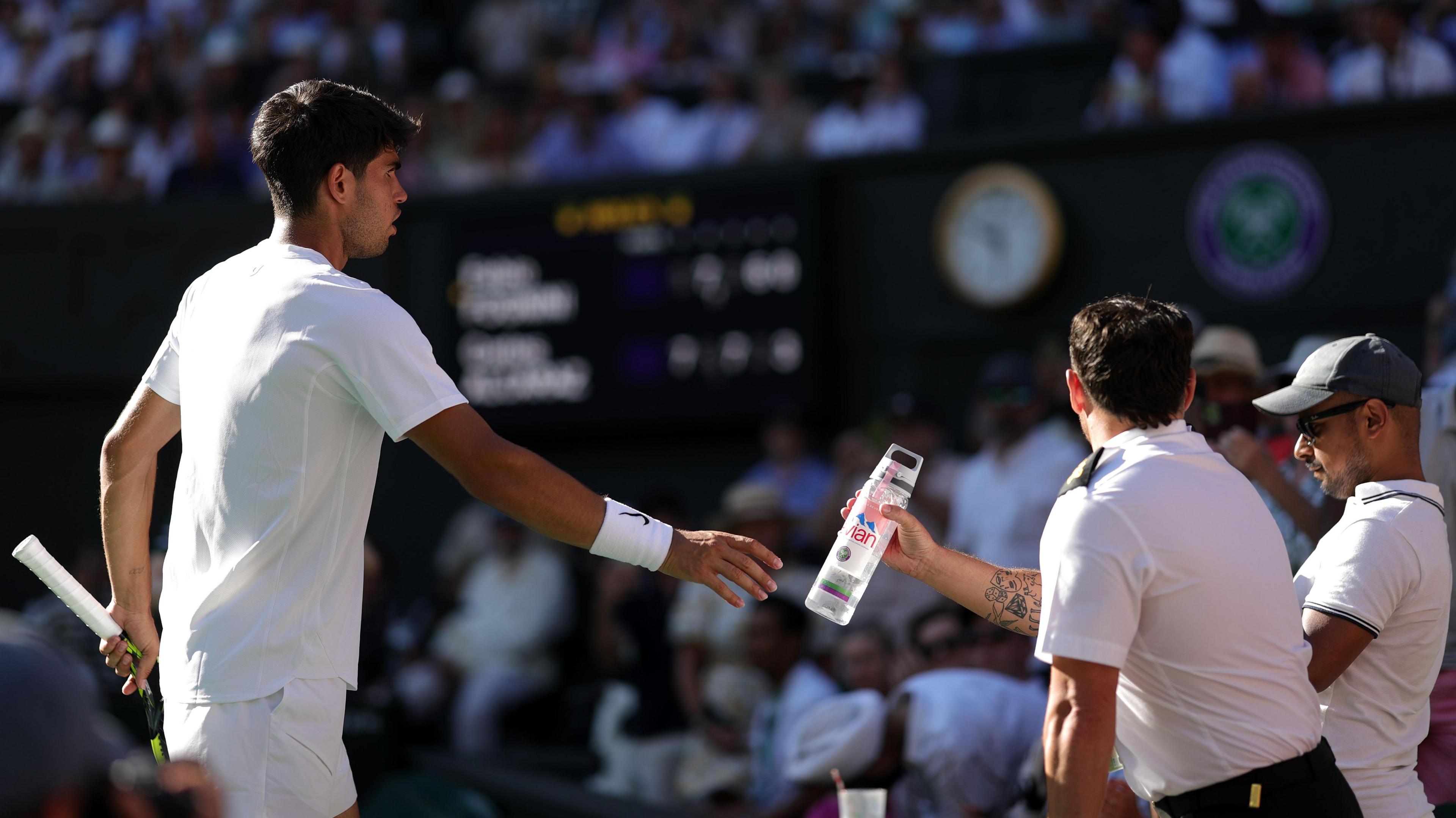 Carlos Alcaraz hands over a bottle of water to a Wimbledon steward