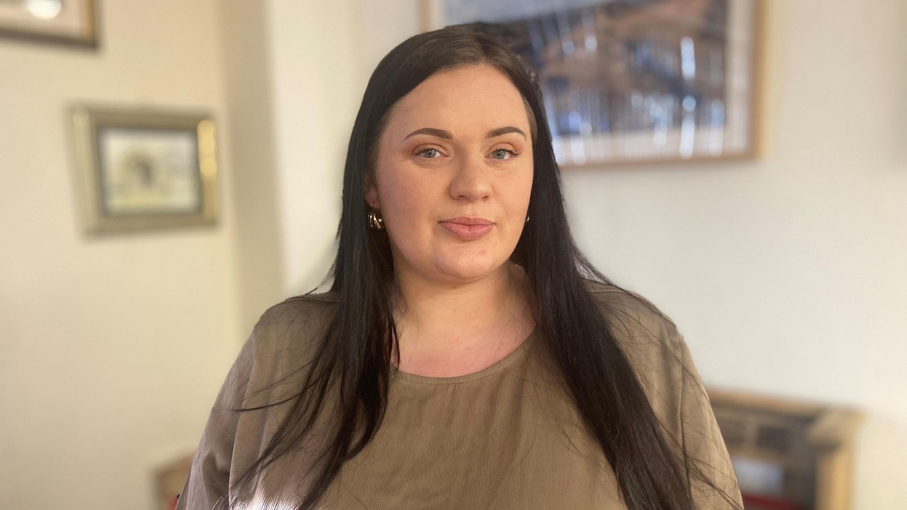 Fiona Goddard, who has long dark hair and wears a brown top, looks straight at the camera.