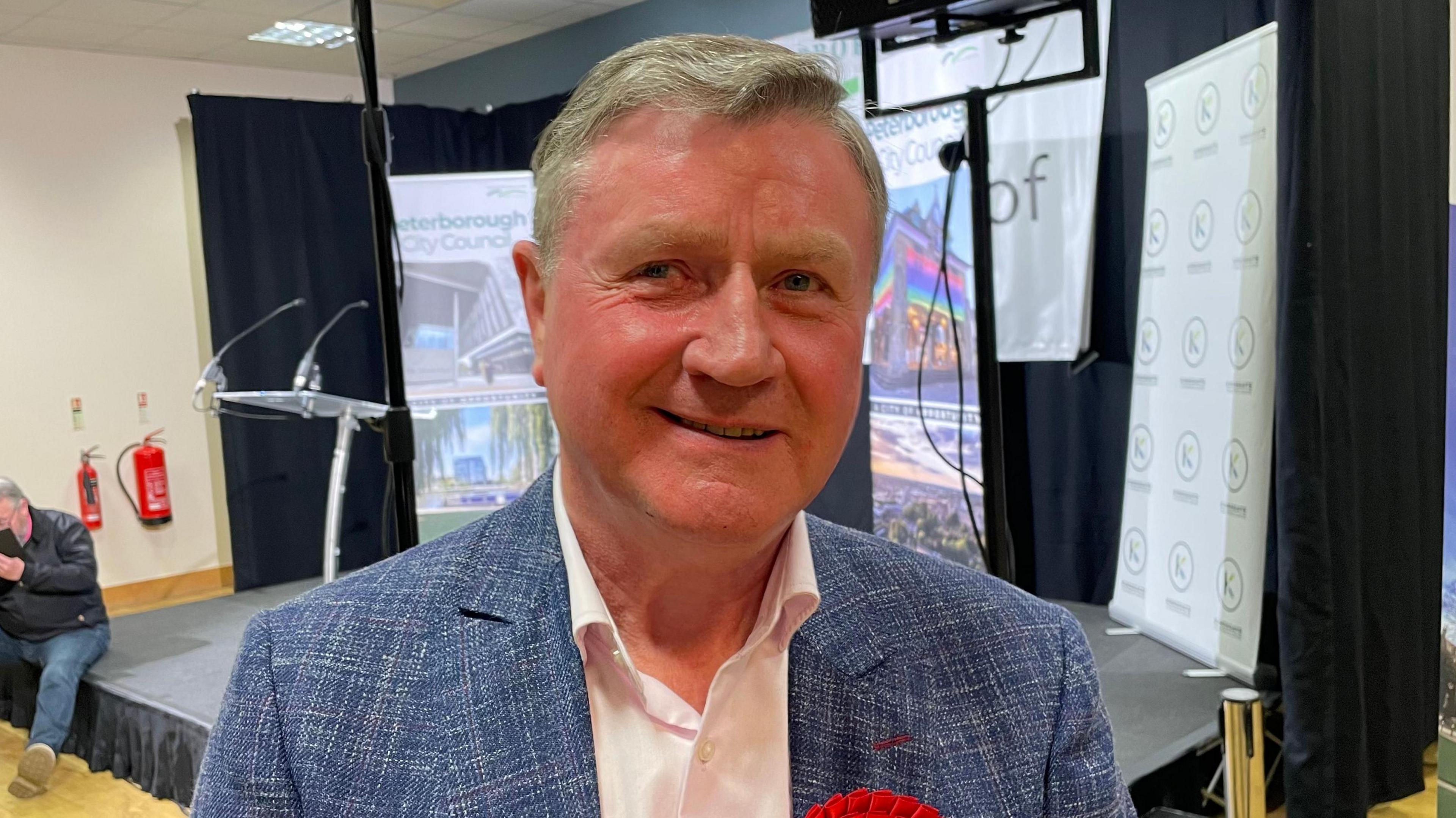 Profile picture of Dennis Jones. He wears a grey jacket, white shirt and a labour party rosette.