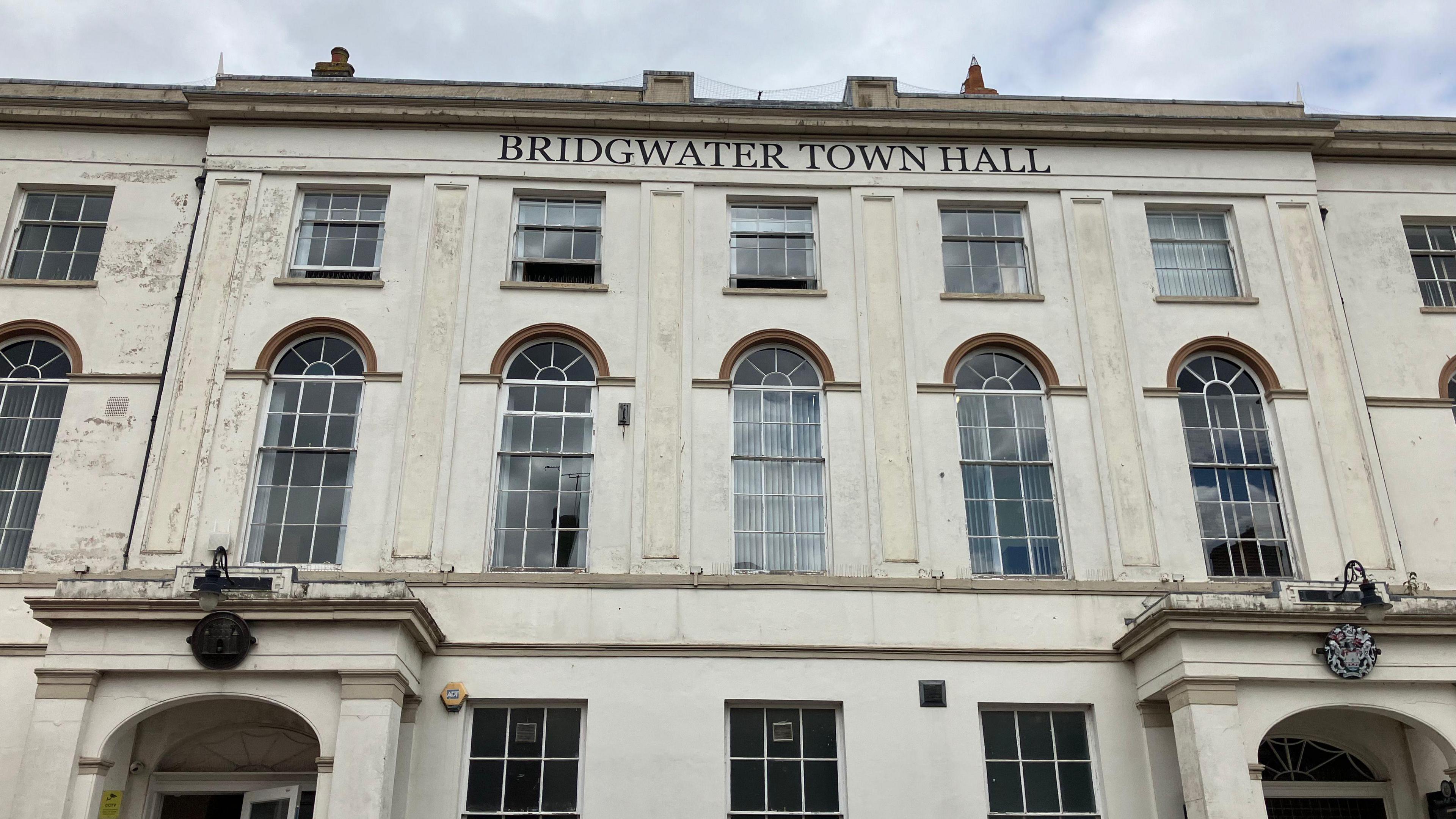 The exterior of cream stone coloured building with 'Bridgwater Town Hall' written in black lettering at the top and big glass windows.