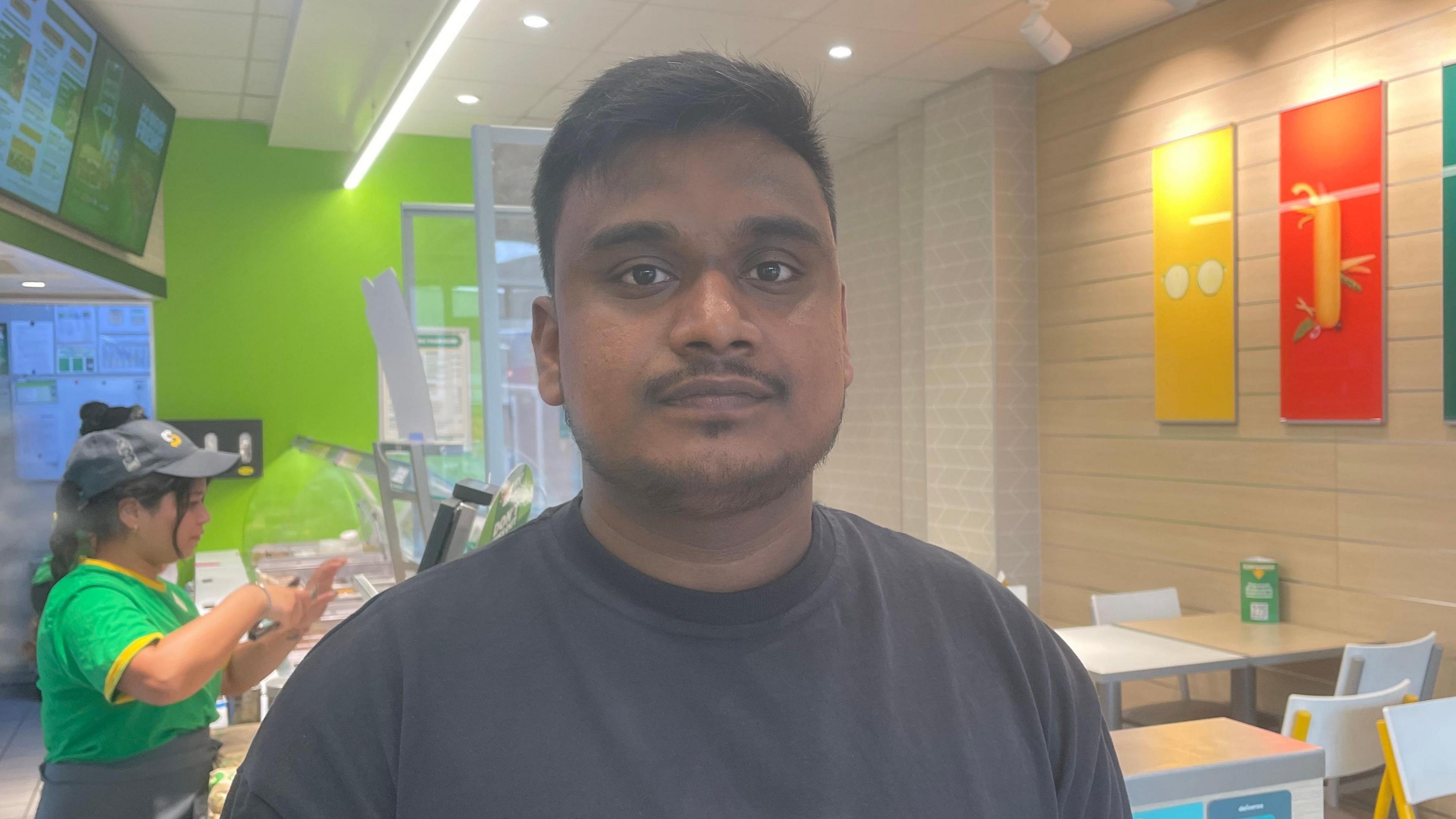 Naani Shaik stood in his subway store in front of the counter with staff stood behind him serving