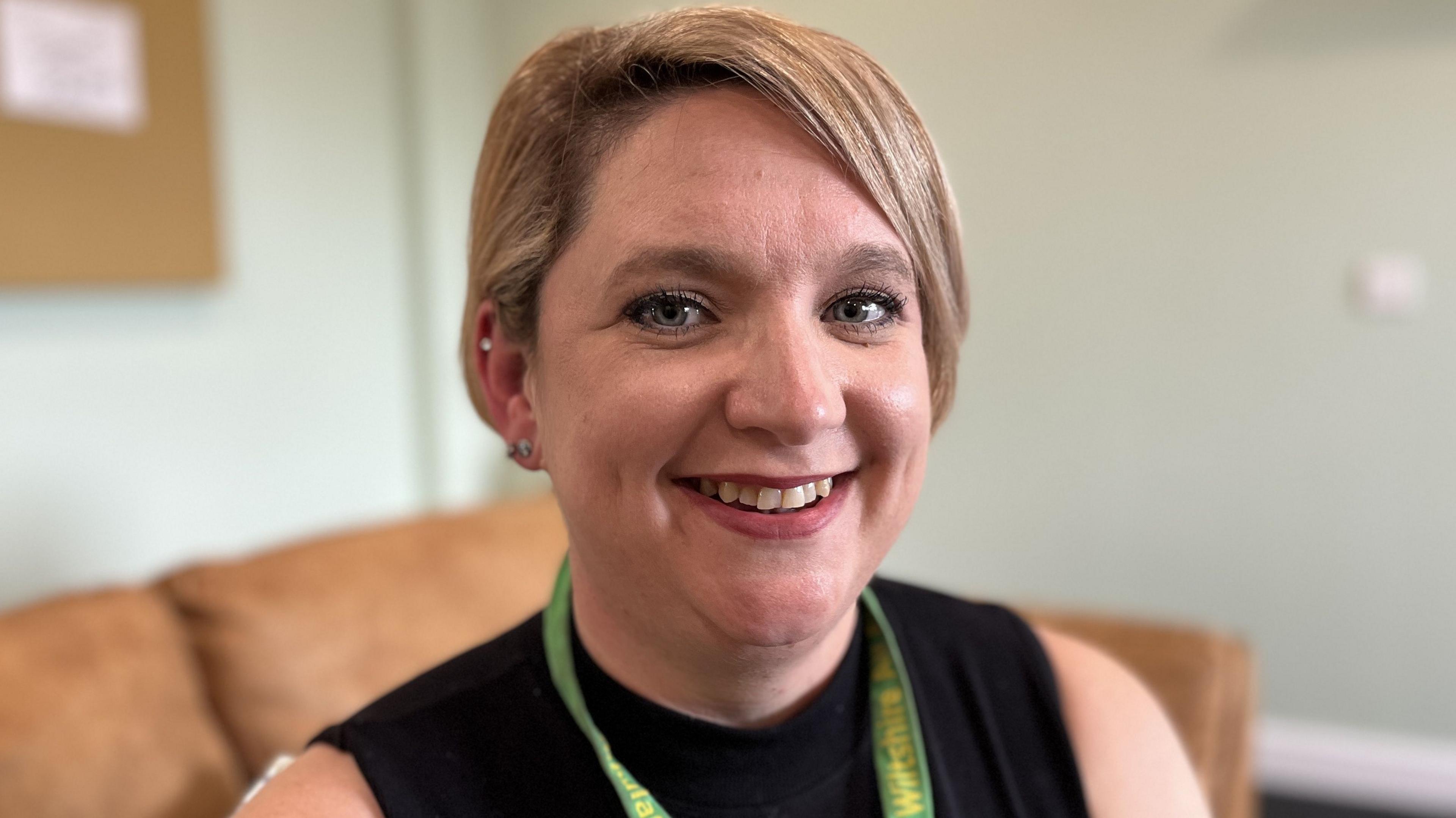 Katy Burke with short blonde hair smiling whilst sat on a sofa in the charity's family room