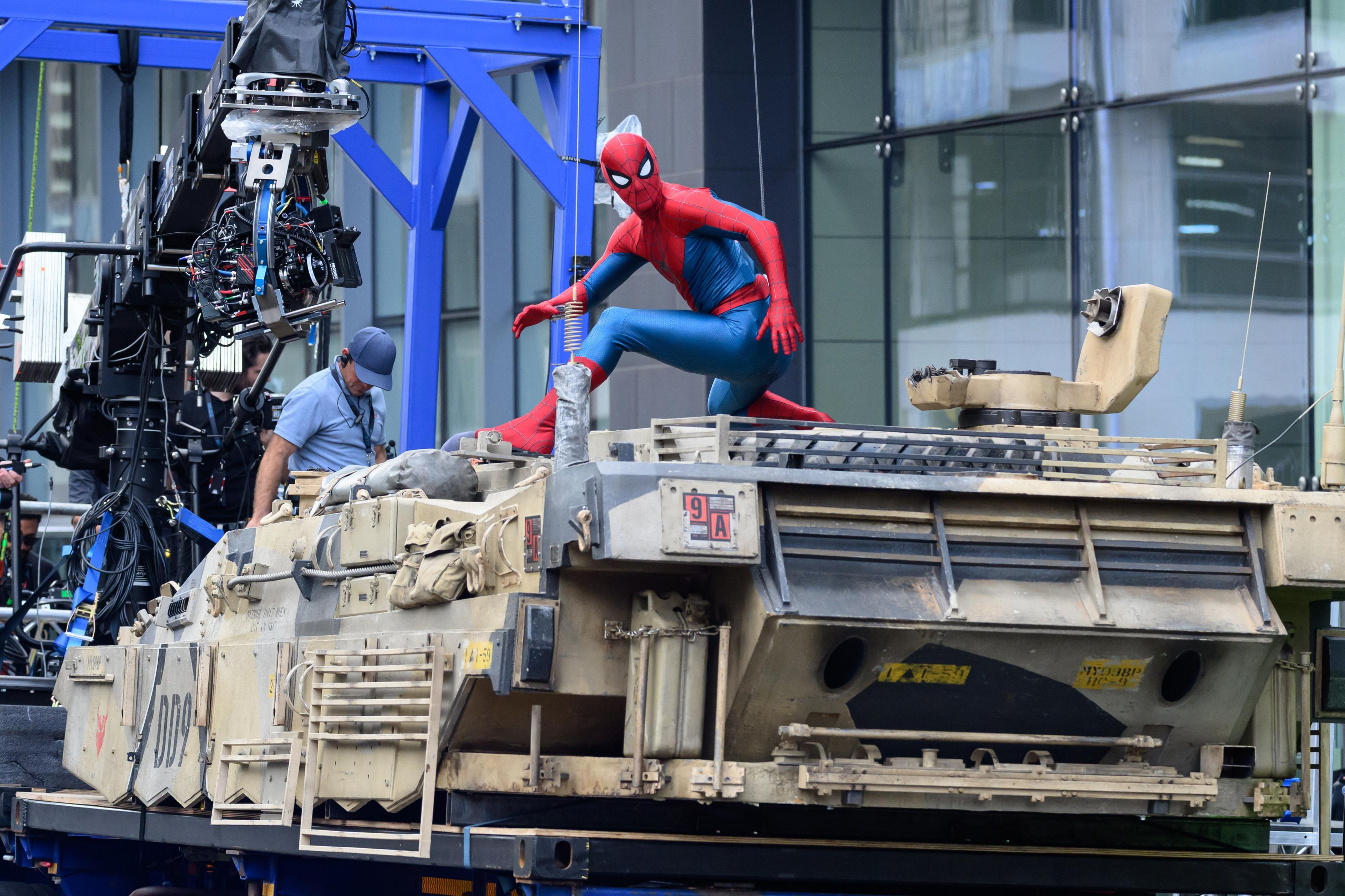 Spider-Man sitting on a tank with a camera crew on the front of it.