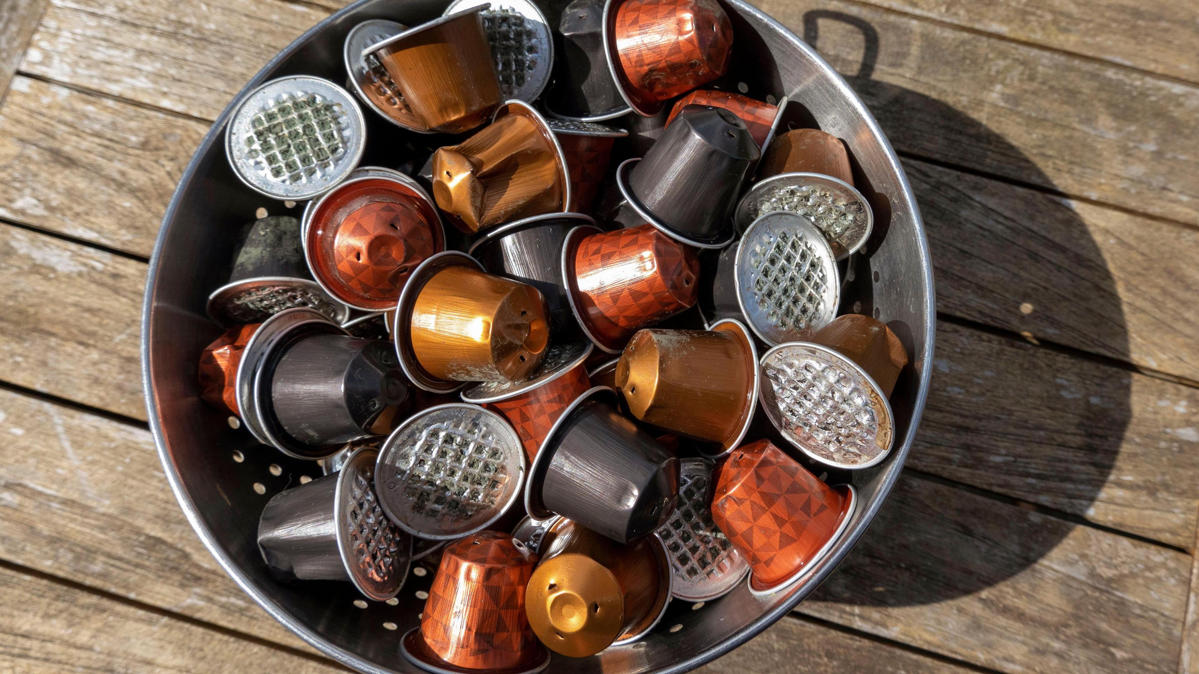 Used coffee capsules ready for the aluminium tops to be recycled. They are collected in a bin that is placed on top of a wooden surface outside on a sunny day