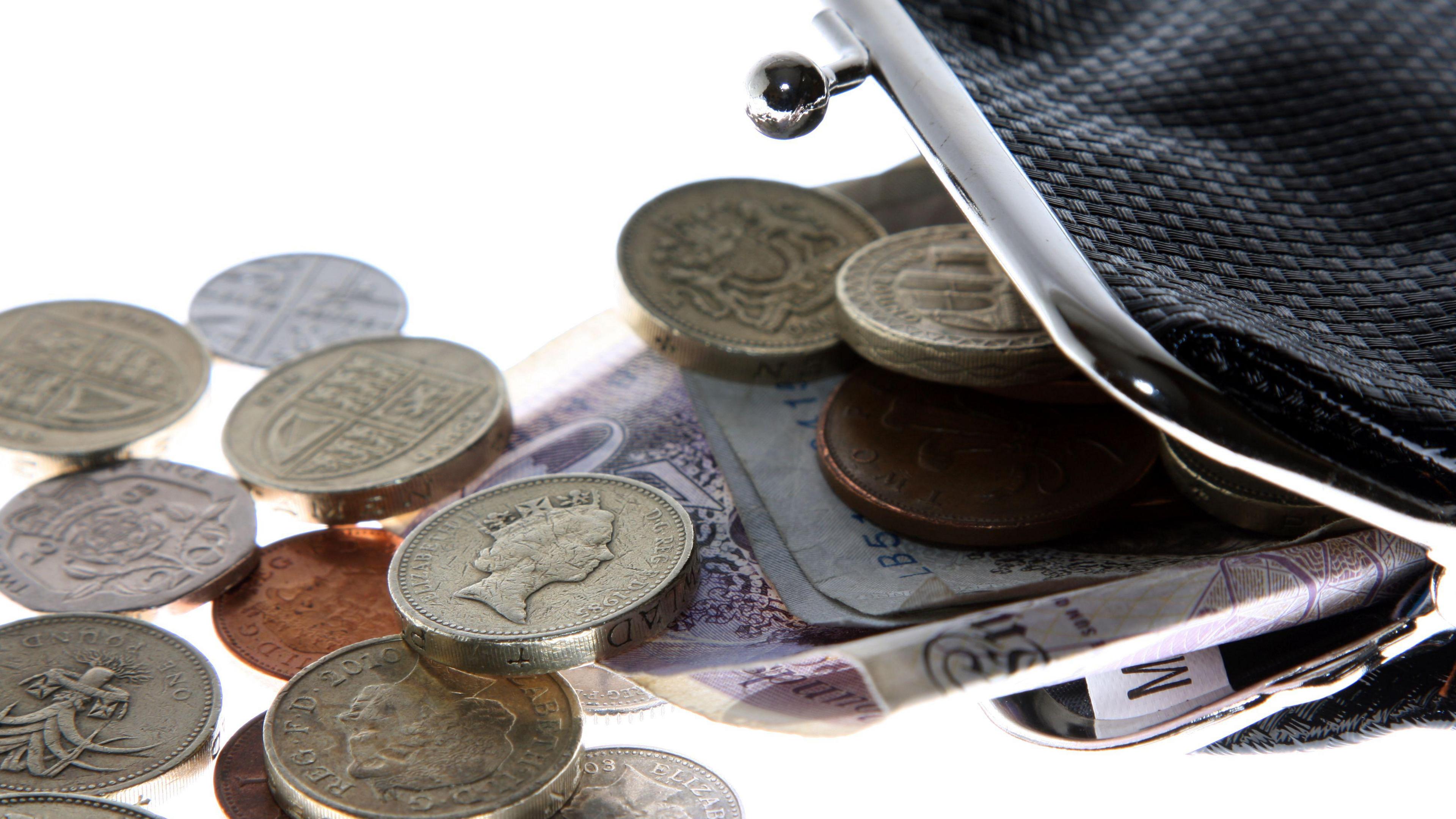 A black purse with the clasp open and money spilling out.