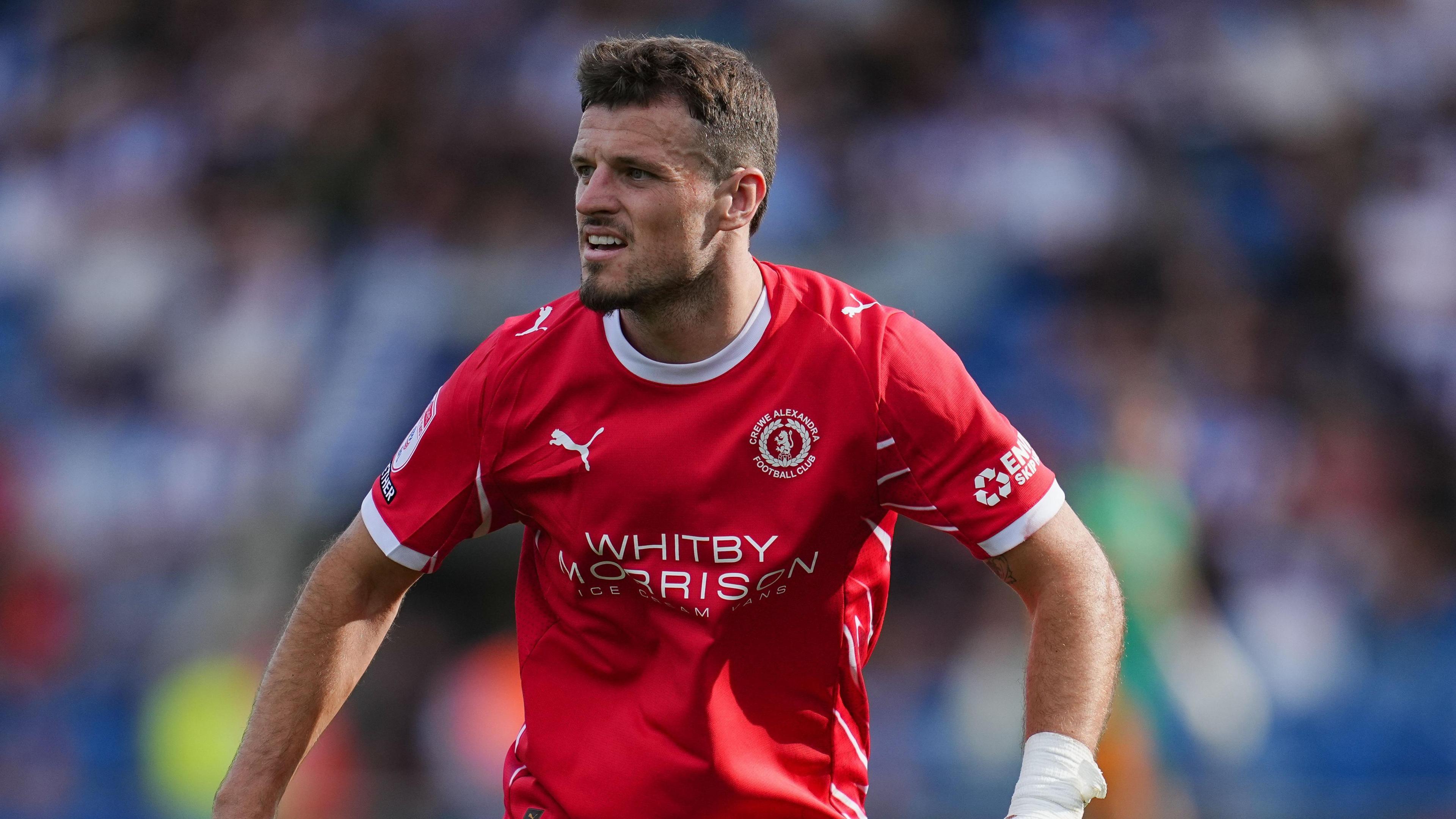 Josh March in action for Crewe in the club's red home shirt. He has a white bandage on his left wrist.