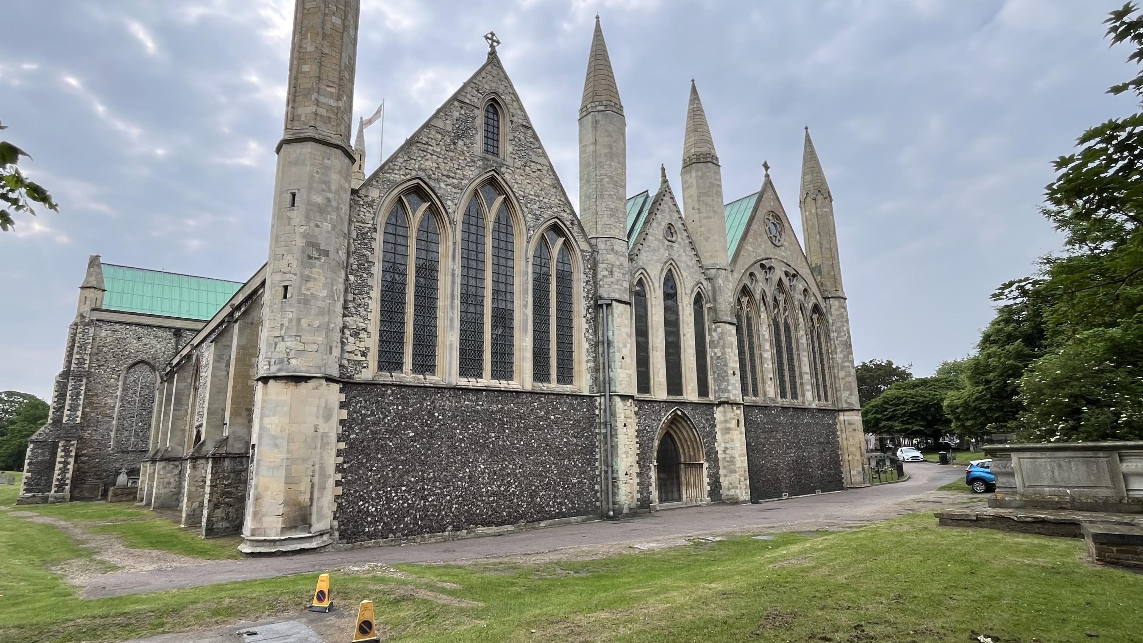 A stone and flint church building with a green copper roof stands in a grassy churchyard.