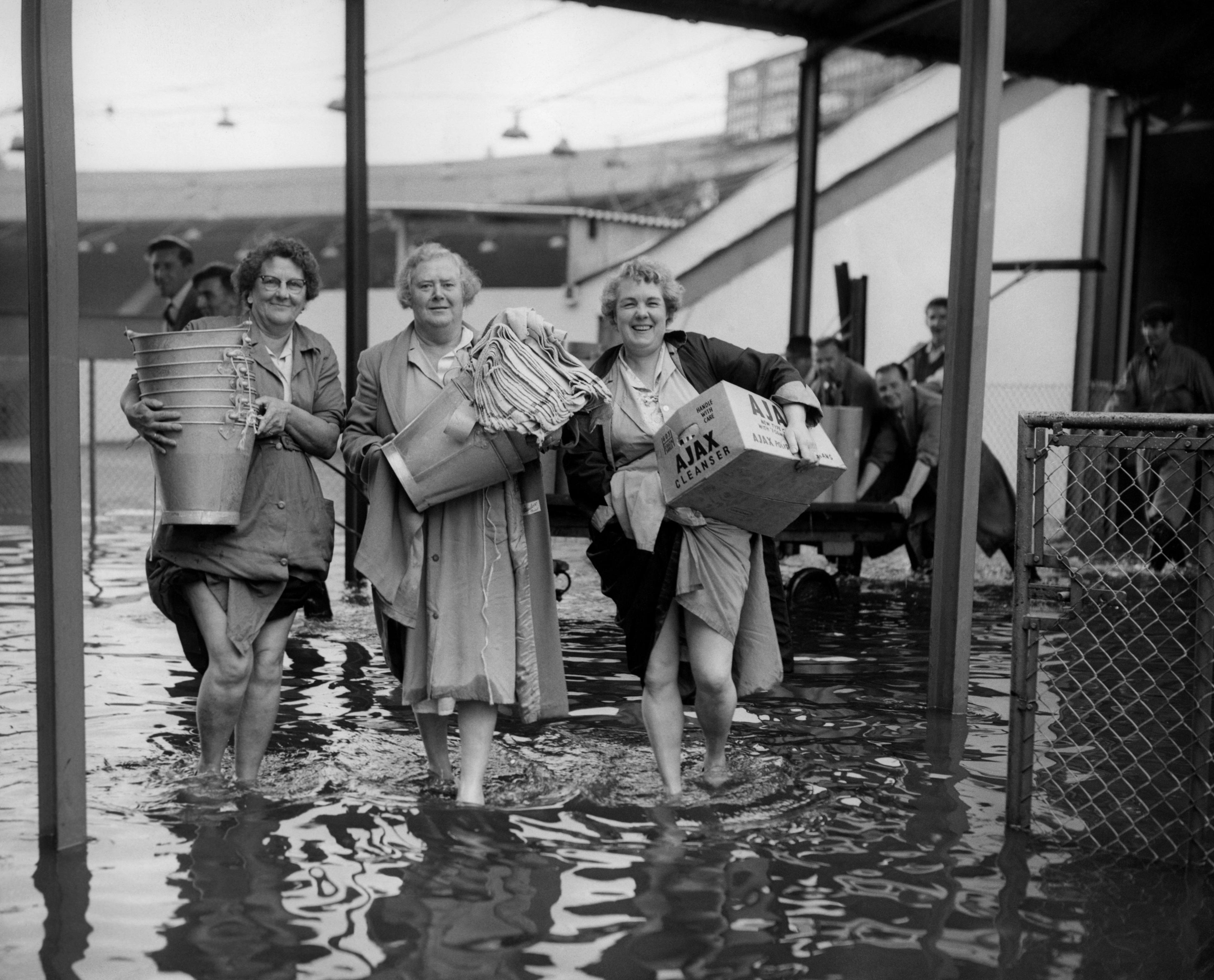 Laden with pails and cloths, three members of the catering staff paddle through the flooded Wimbledon Stadium.