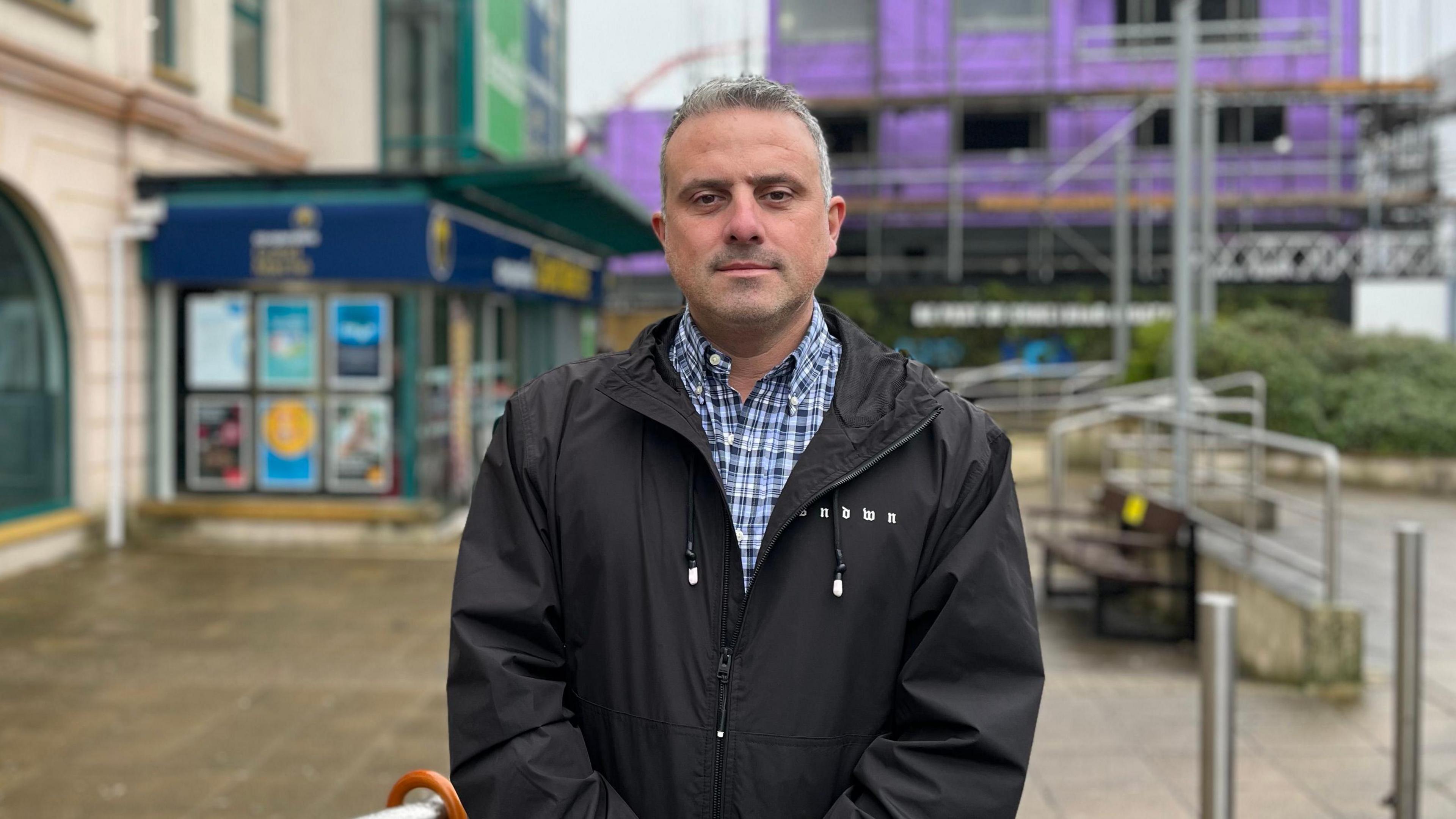 A man wearing a coat outside a shopping centre.
