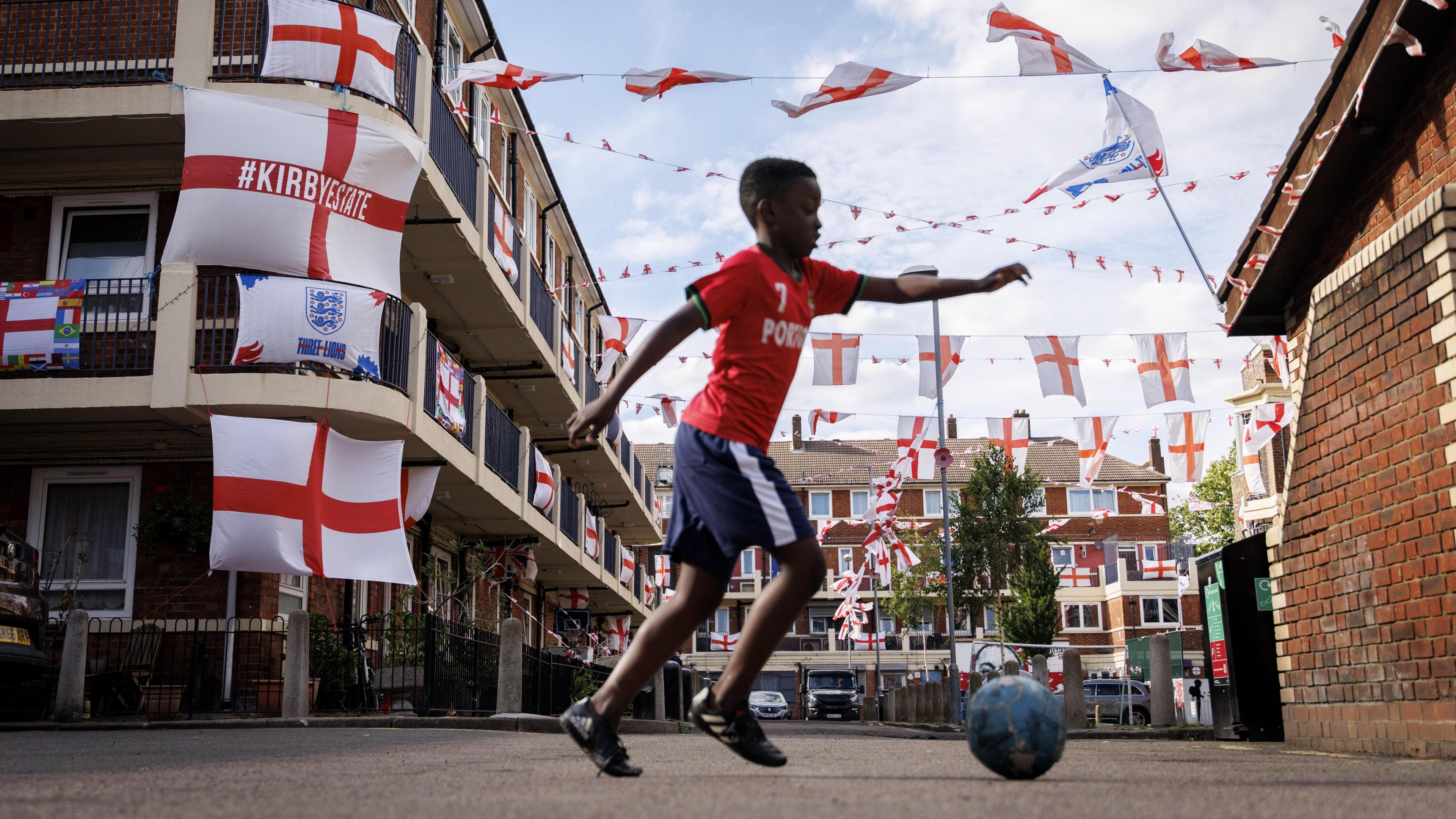 A boy plays football in a housing estate in London decorated with England flags.