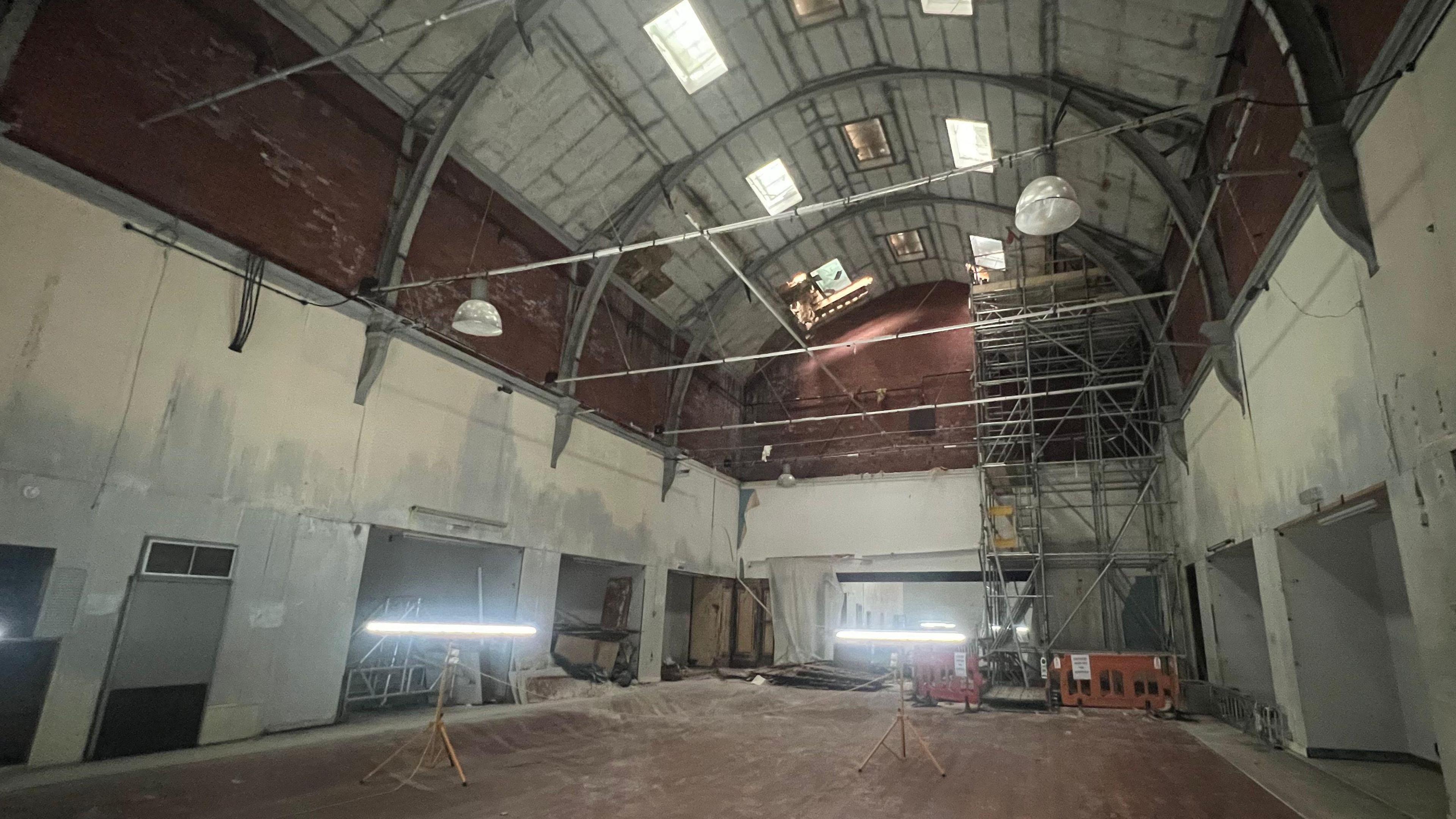 The interior of Jacobs Wells Baths. The large room is dark, lit only by industrial electric lighting, and and has a very high vaulted ceiling. 