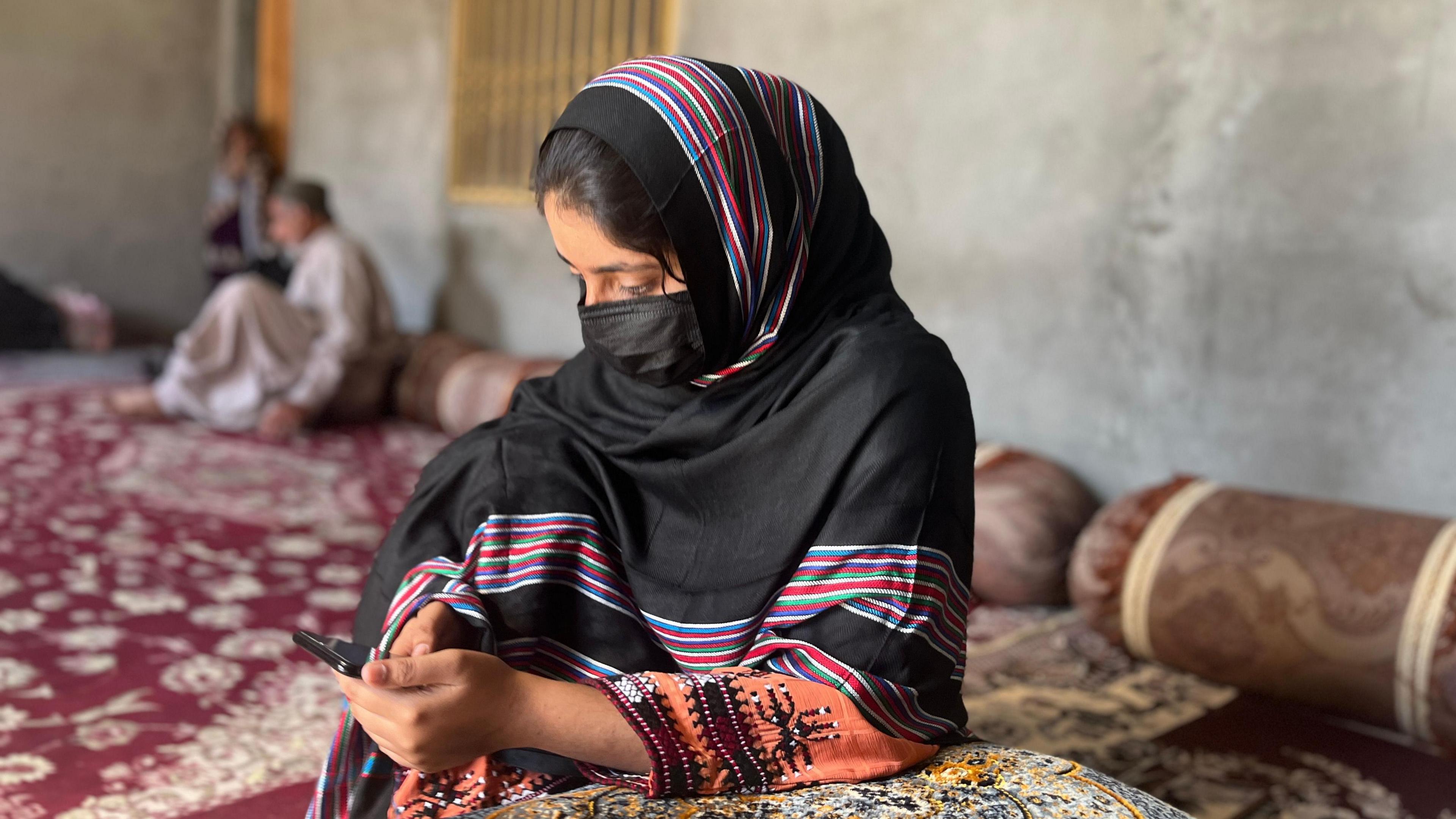 Saira looks at her phone while leaning on a cushion. 