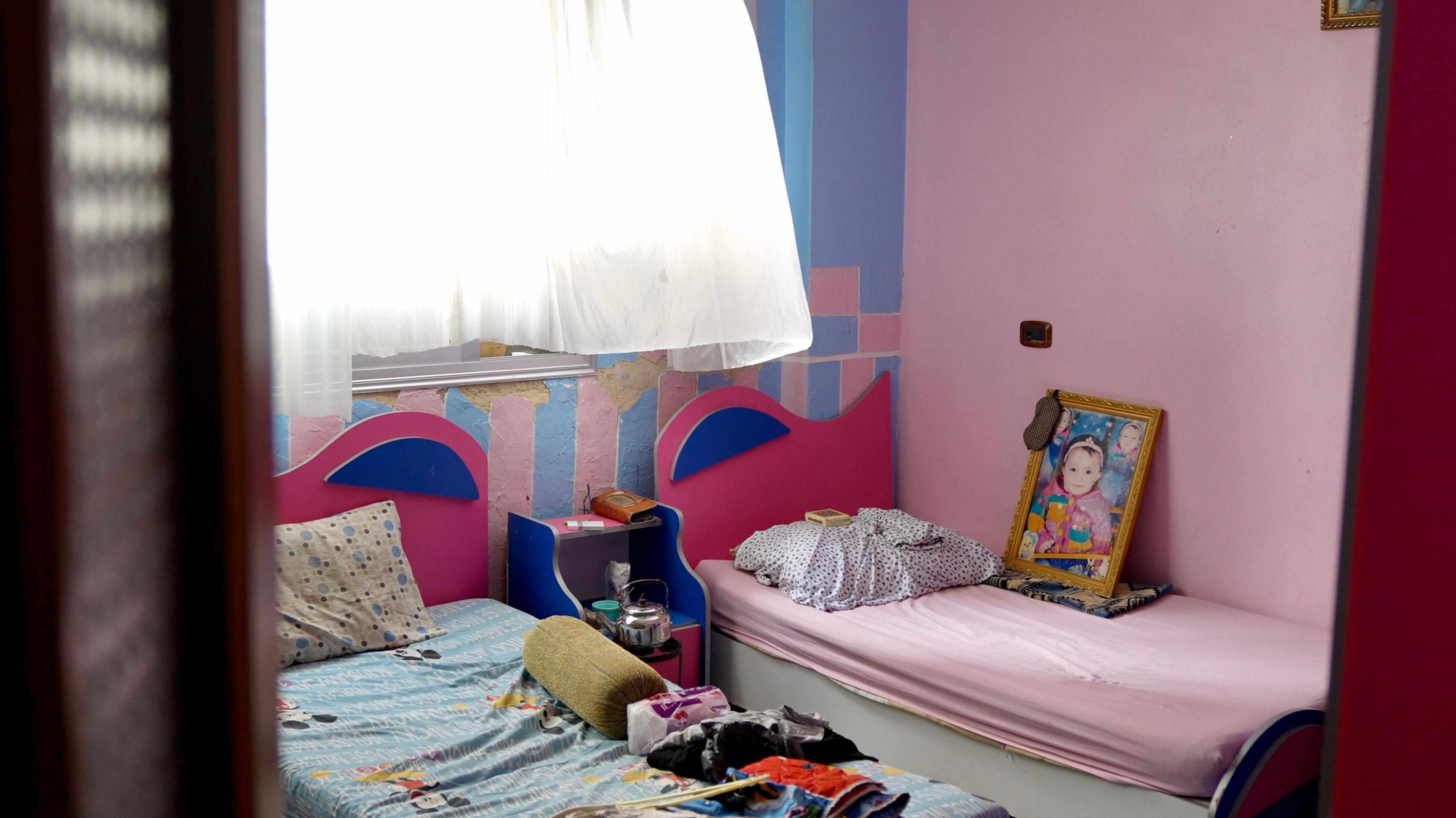 A child's bedroom is seen with blue and pink walls, two beds and a large framed image of a little girl