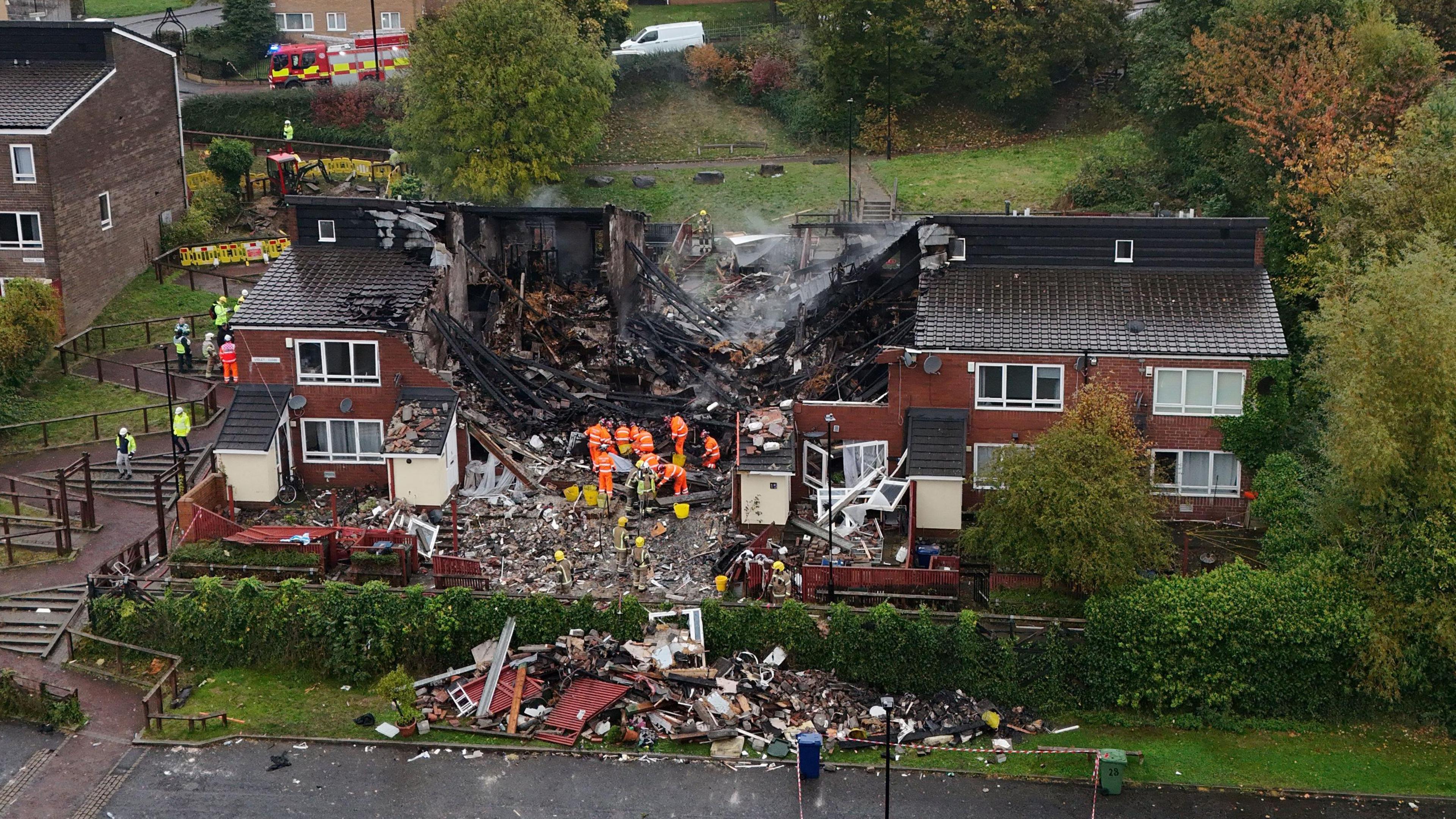 Firefighters on site at the explosion. The houses in the centre have been ripped apart and there is debris on the ground.
