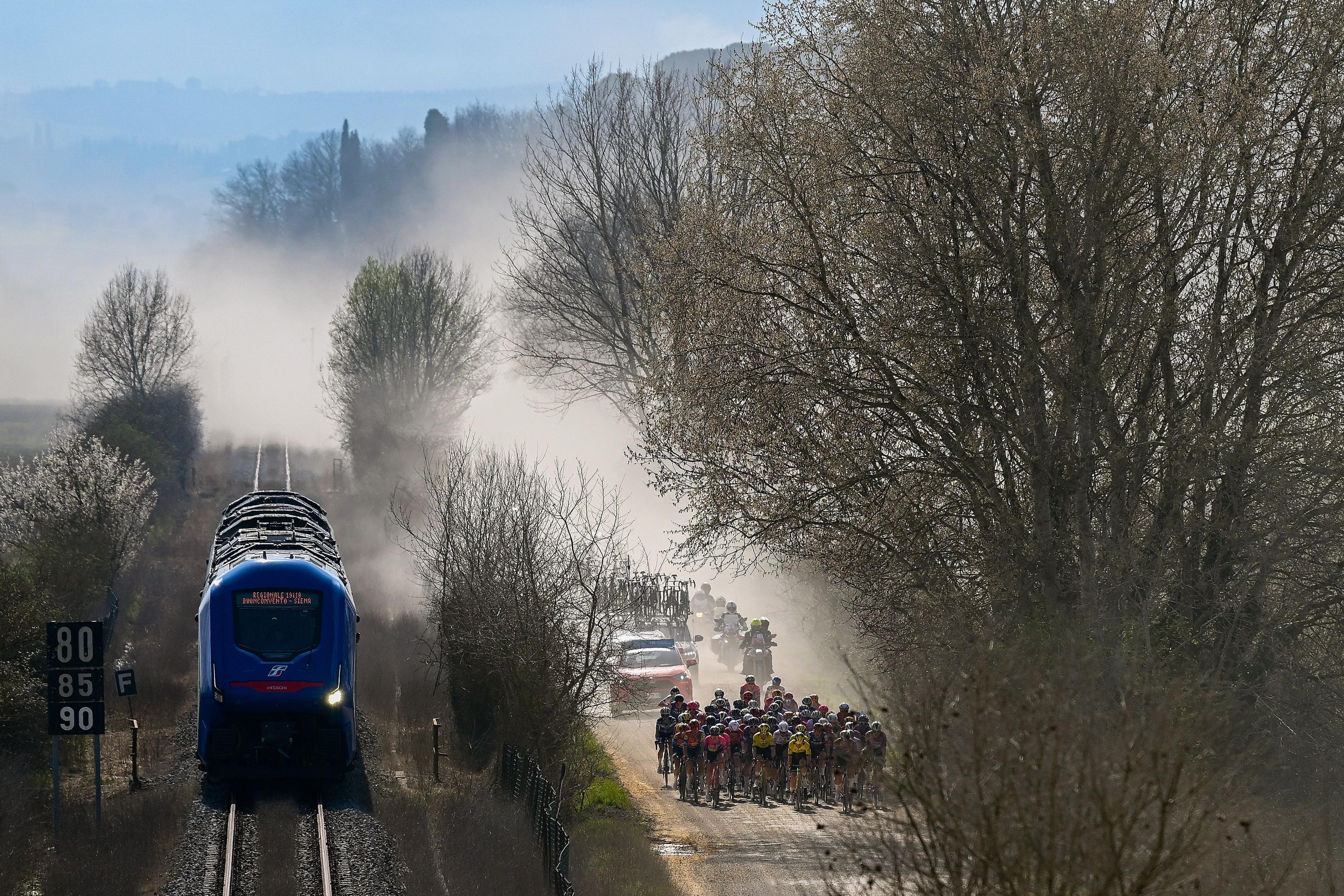 Cyclists alongside a moving train during the women's edition of Strade Bianche in Siena, Italy
