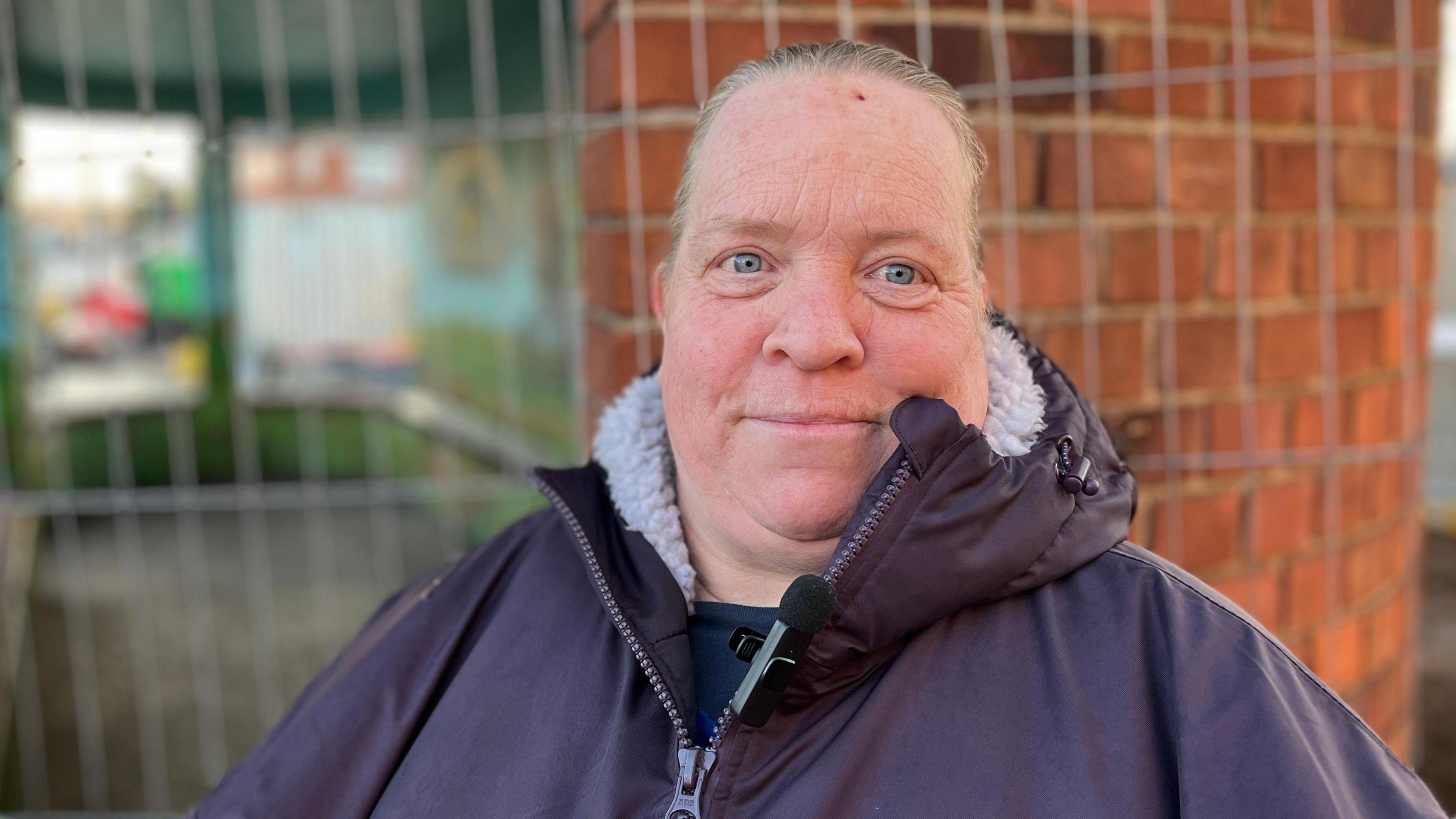 A woman with her hair in a ponytail smiling at the camera. She is wearing a big thick winter coat. 
