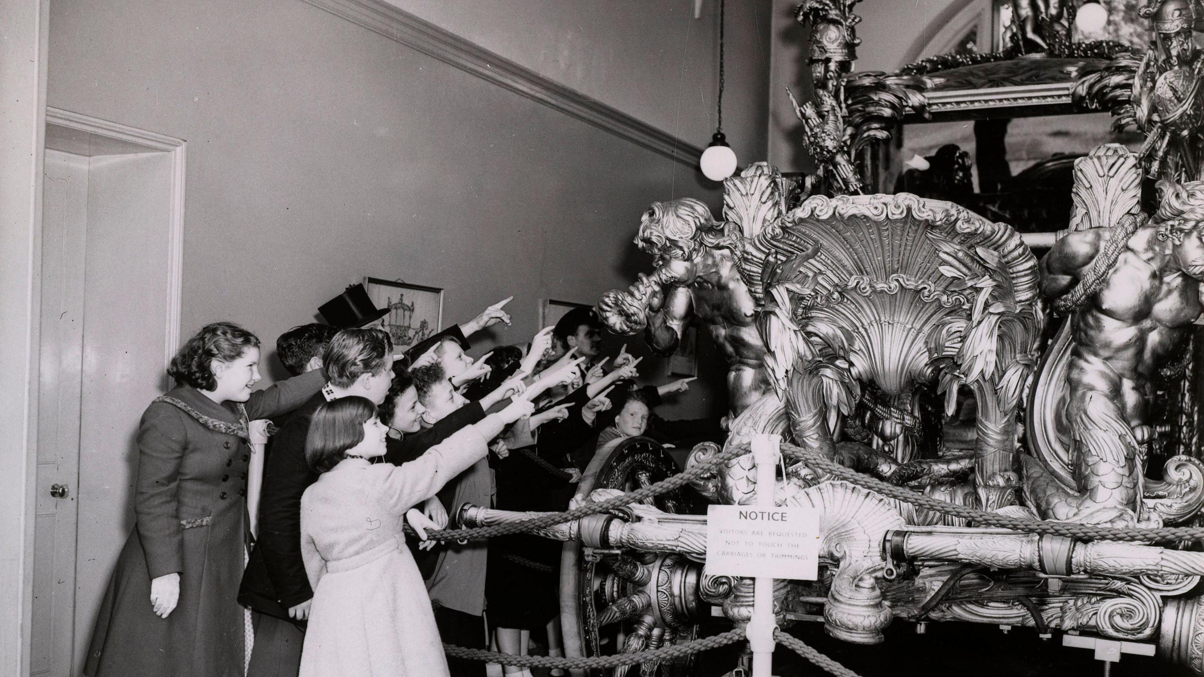 A group of young people all pointing at the Gold Coach in a staged photo taking circa 1953.