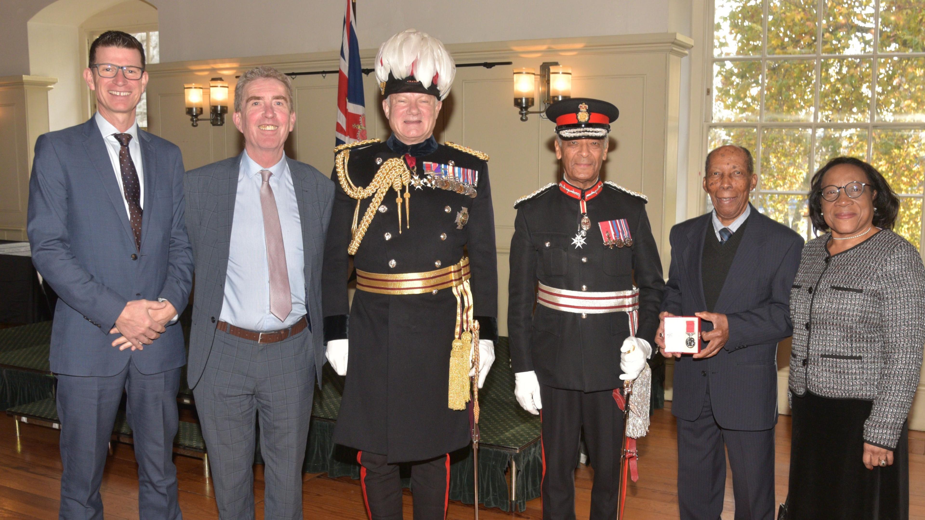 A group picture of six people - five men and one woman - all wearing smart clothes and suits. They are stood in a room with white walls and there is a large window with lots of greenery outside. 