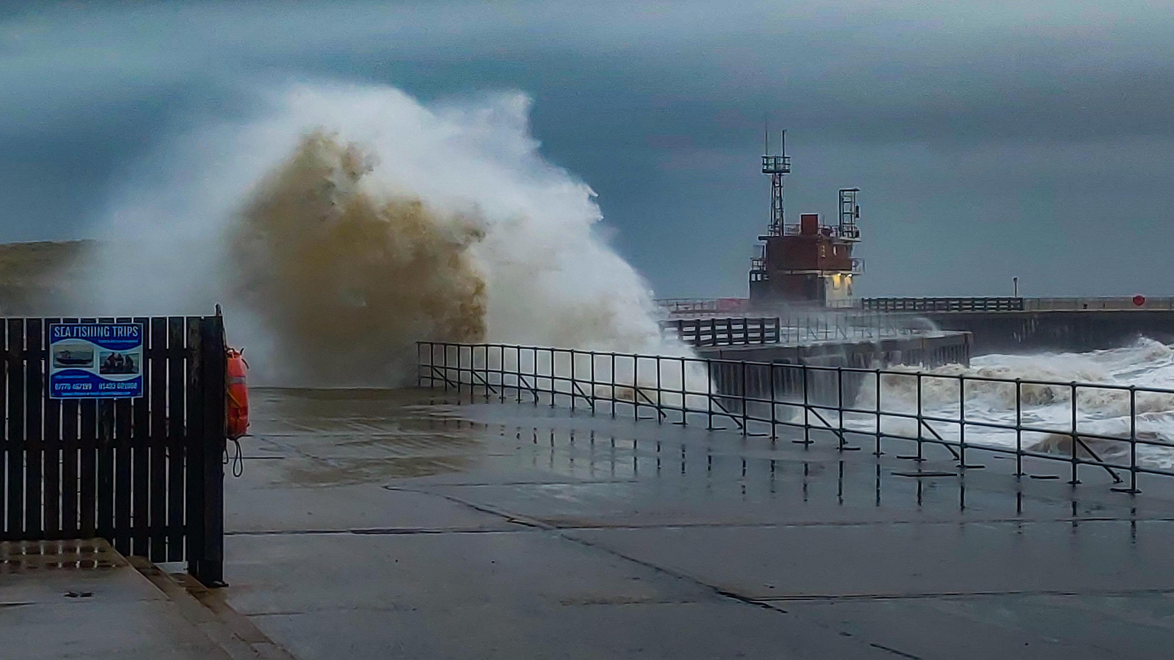 Large waves at Gorleston-on-Sea, Norfolk, showing a seafront, a small fence and sea barriers.