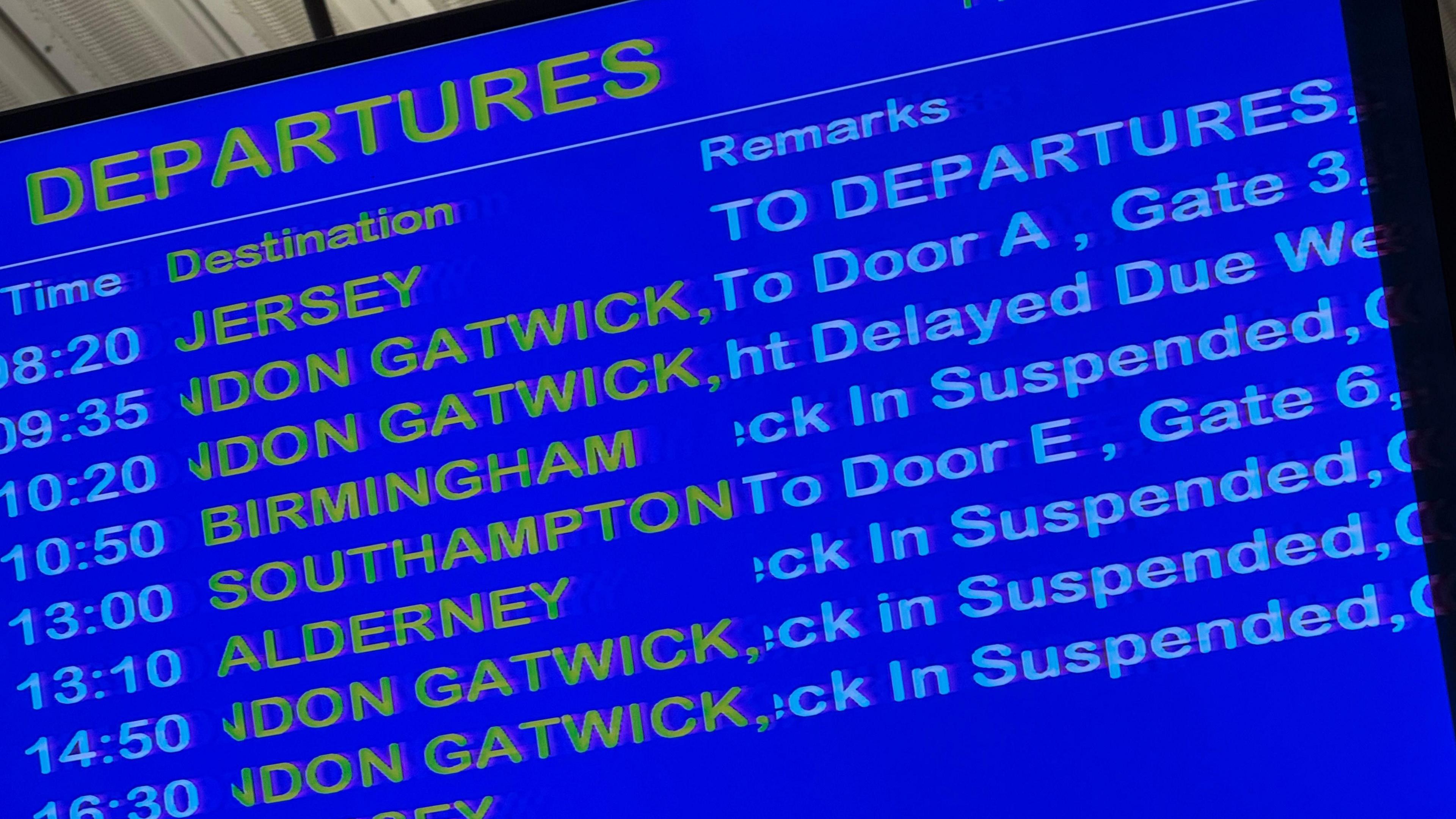 A departure board at Guernsey Airport. It is blue with times on the left, location in the middle and remarks- with the delays- on the right