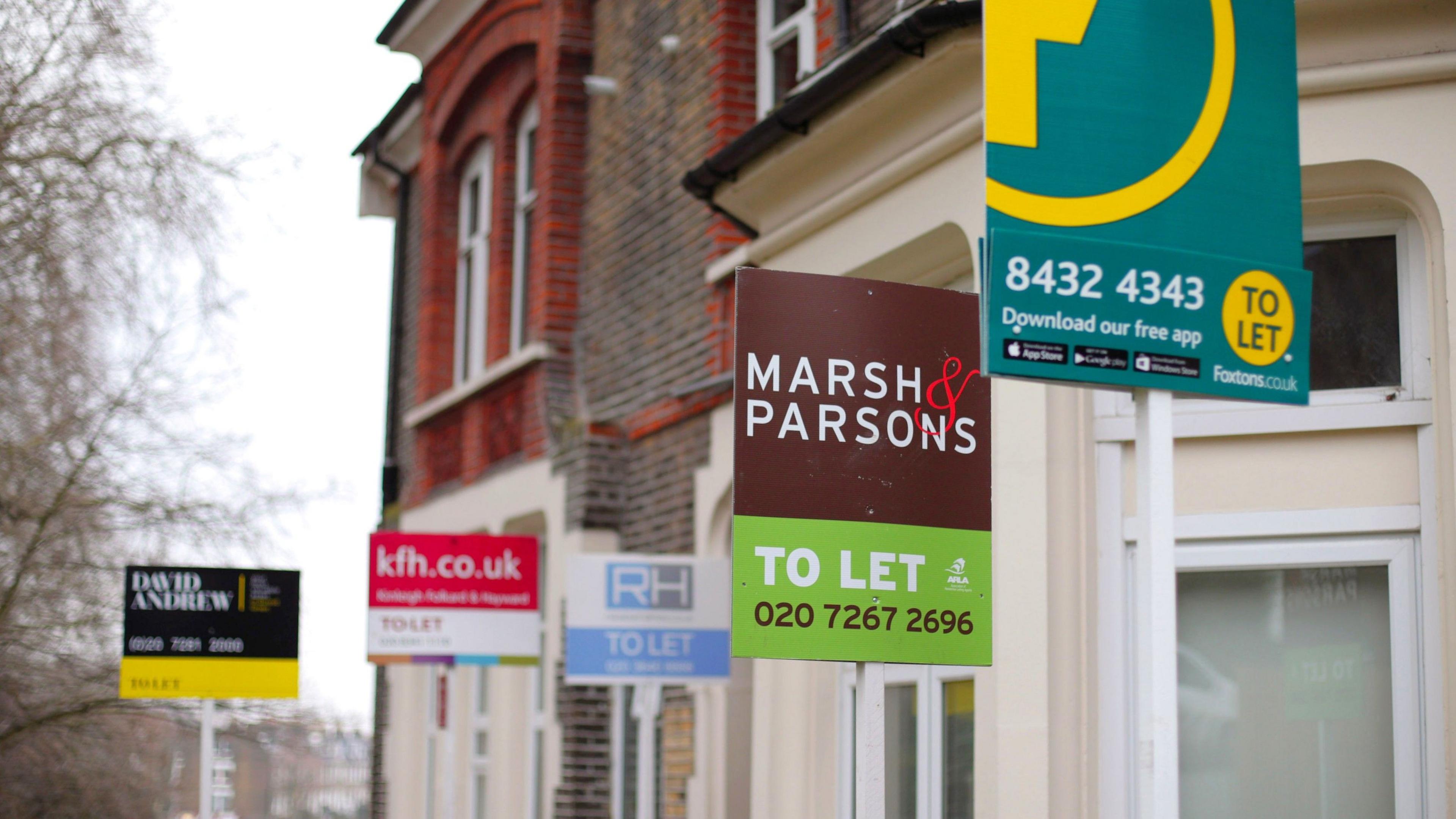 A row of terraced brick properties with 'TO LET' signs outside the front from various different estate agents.