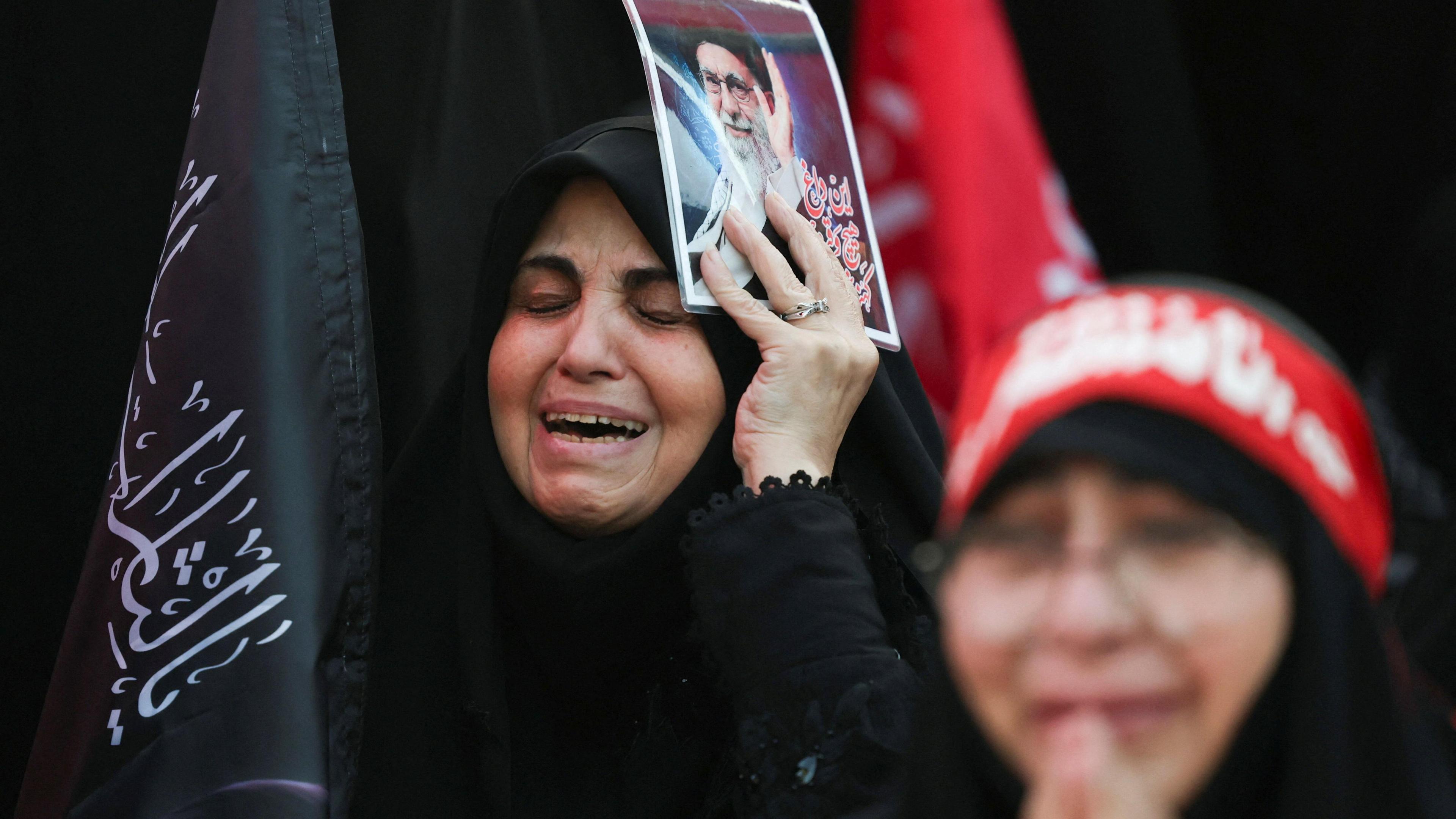 A woman appears to cry as she attends Ayatollah Khamenei's funeral holding a poster of him.