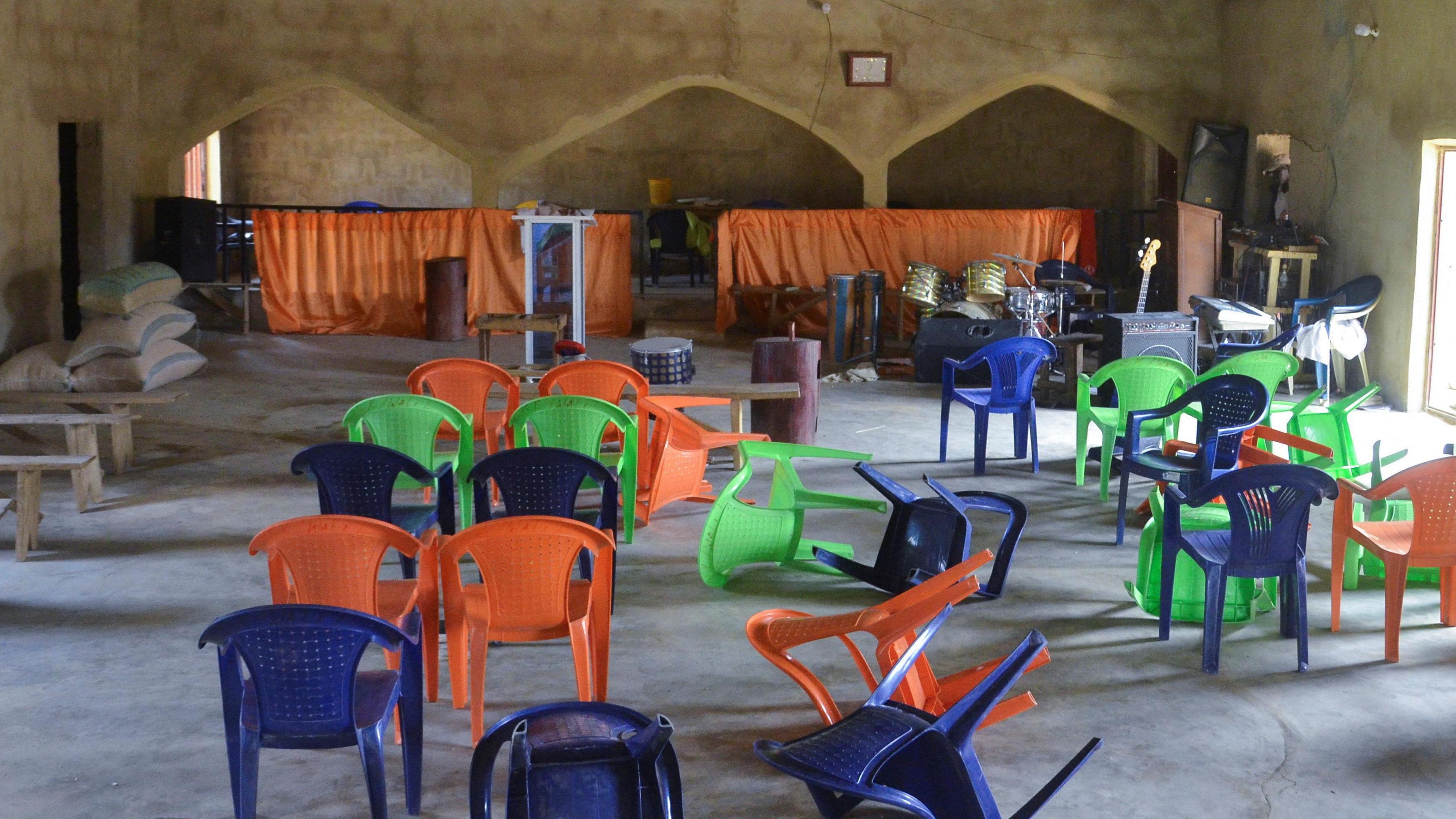 The inside of Haske Cherubim and Seraphim Movement Church, after an attack by gunmen in which worshippers were kidnapped.  There are orange, green and blue plastic chairs scattered on the floor. 