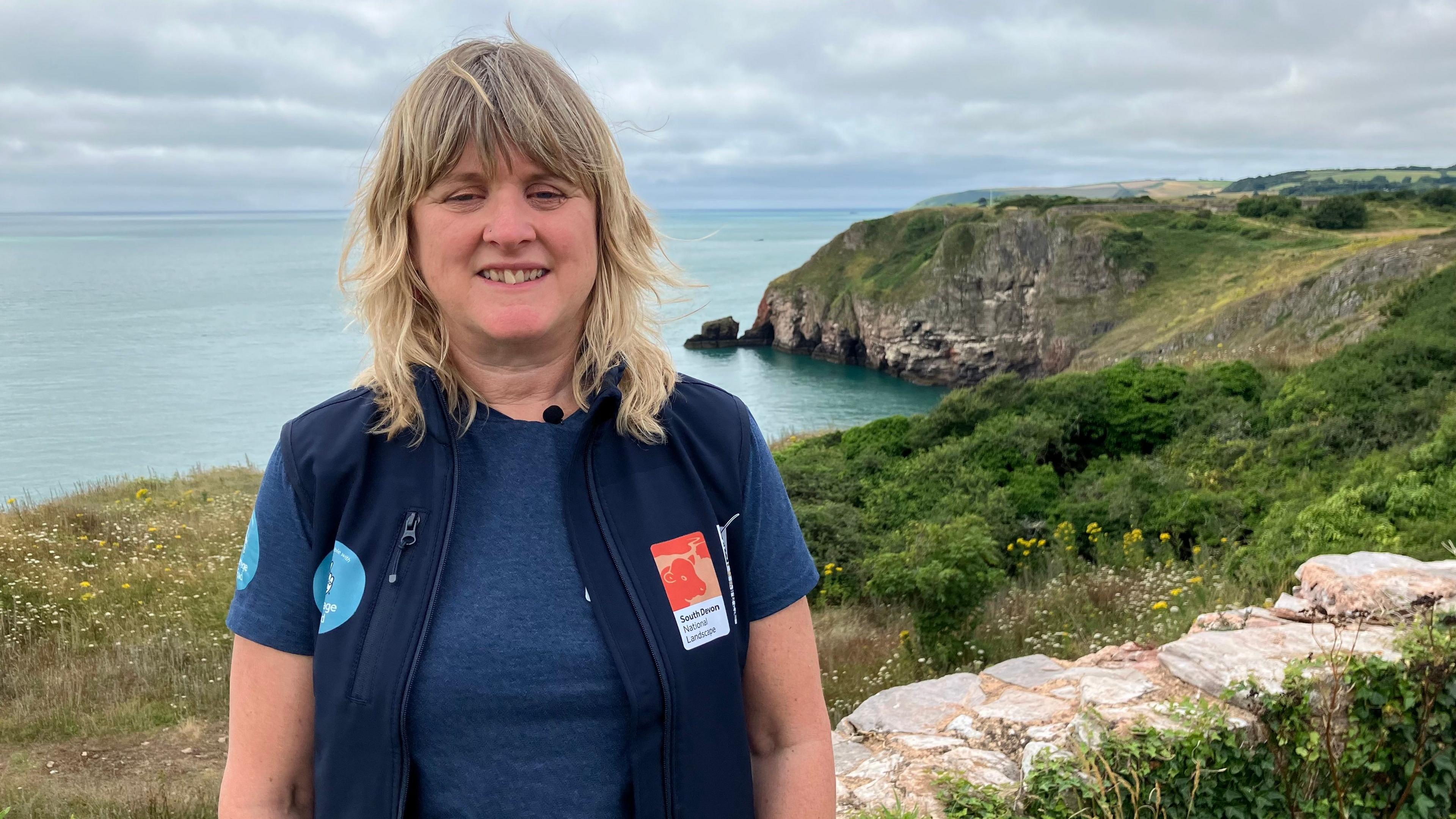 Nicky Bailey looks at the camera while standing in front of a cliff view