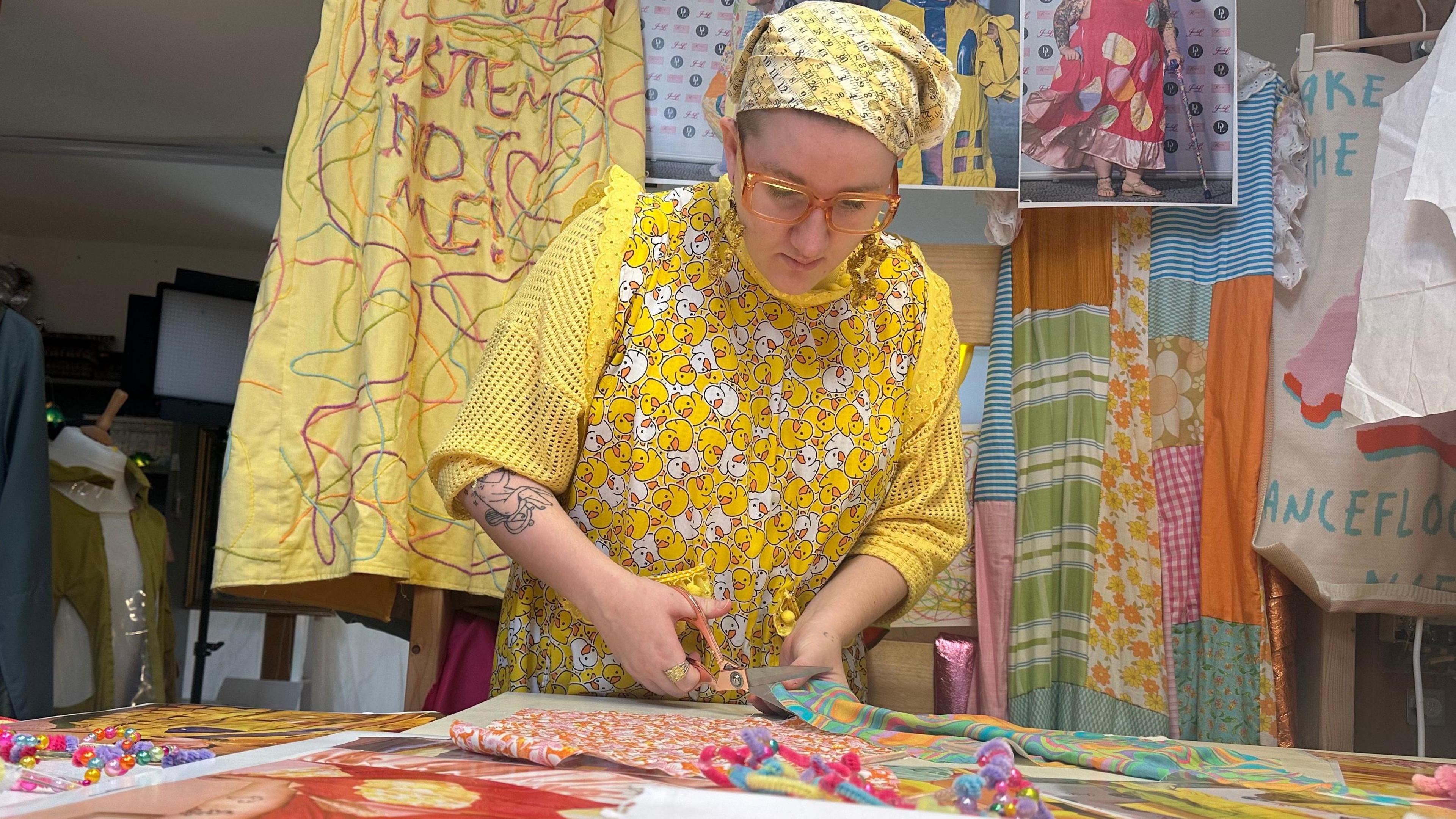 May Gauntlett cutting a piece of fabric on her cutting table in her studio.