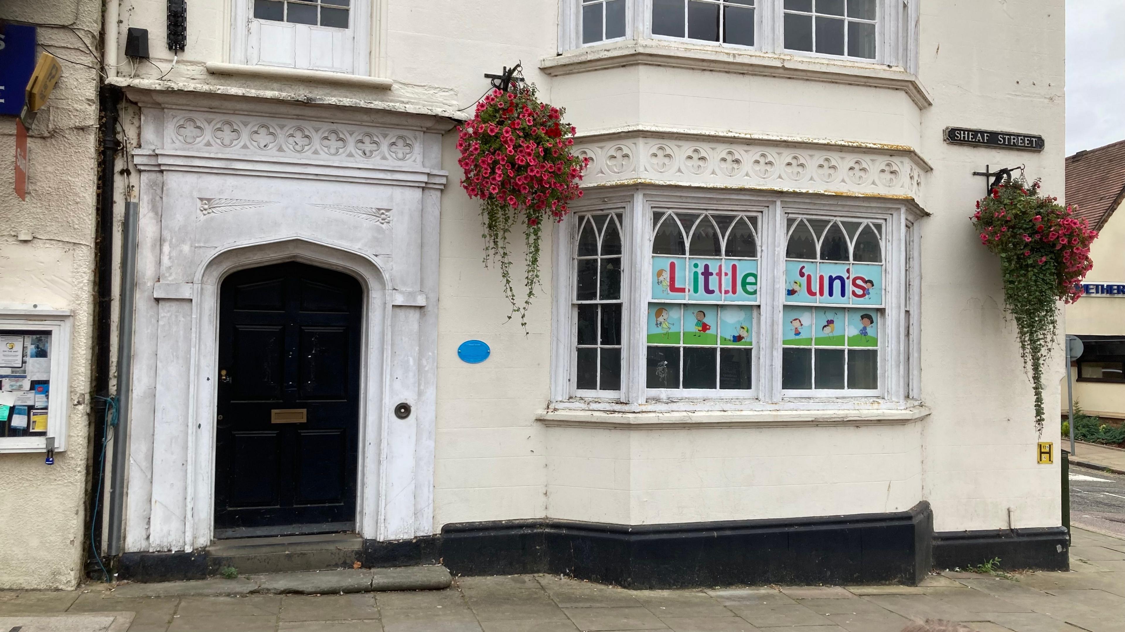 Cream-rendered building with large wooden door and "Little 'un's" sign in window - a blue plaque is visible next to the window