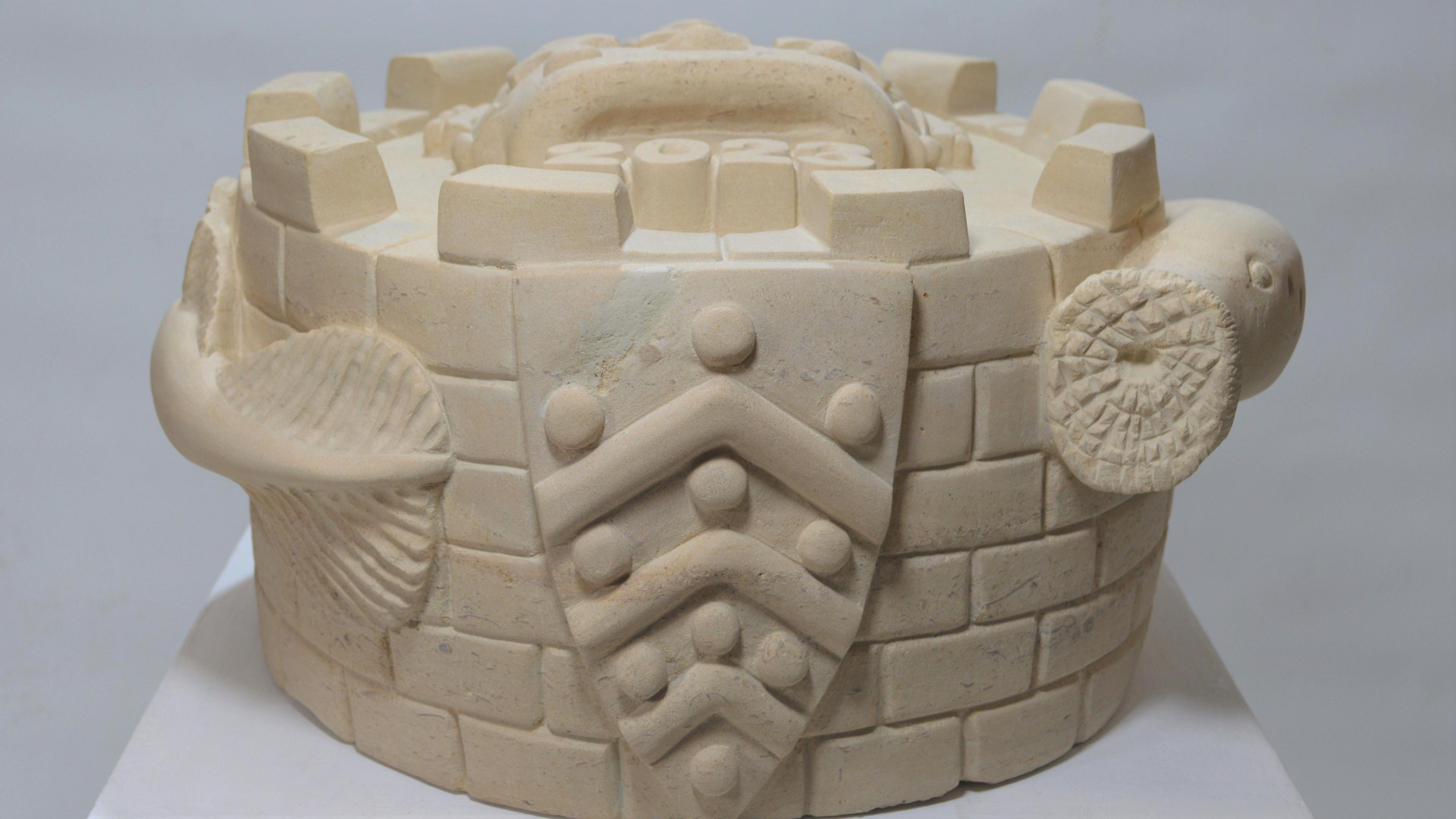 A side view of the stone pie shows a shield and a lamprey snaking around the circumference of the pie, with its sucker-like mouth and tail visible. The pie is sculpted like a castle, with bricks and turrets.