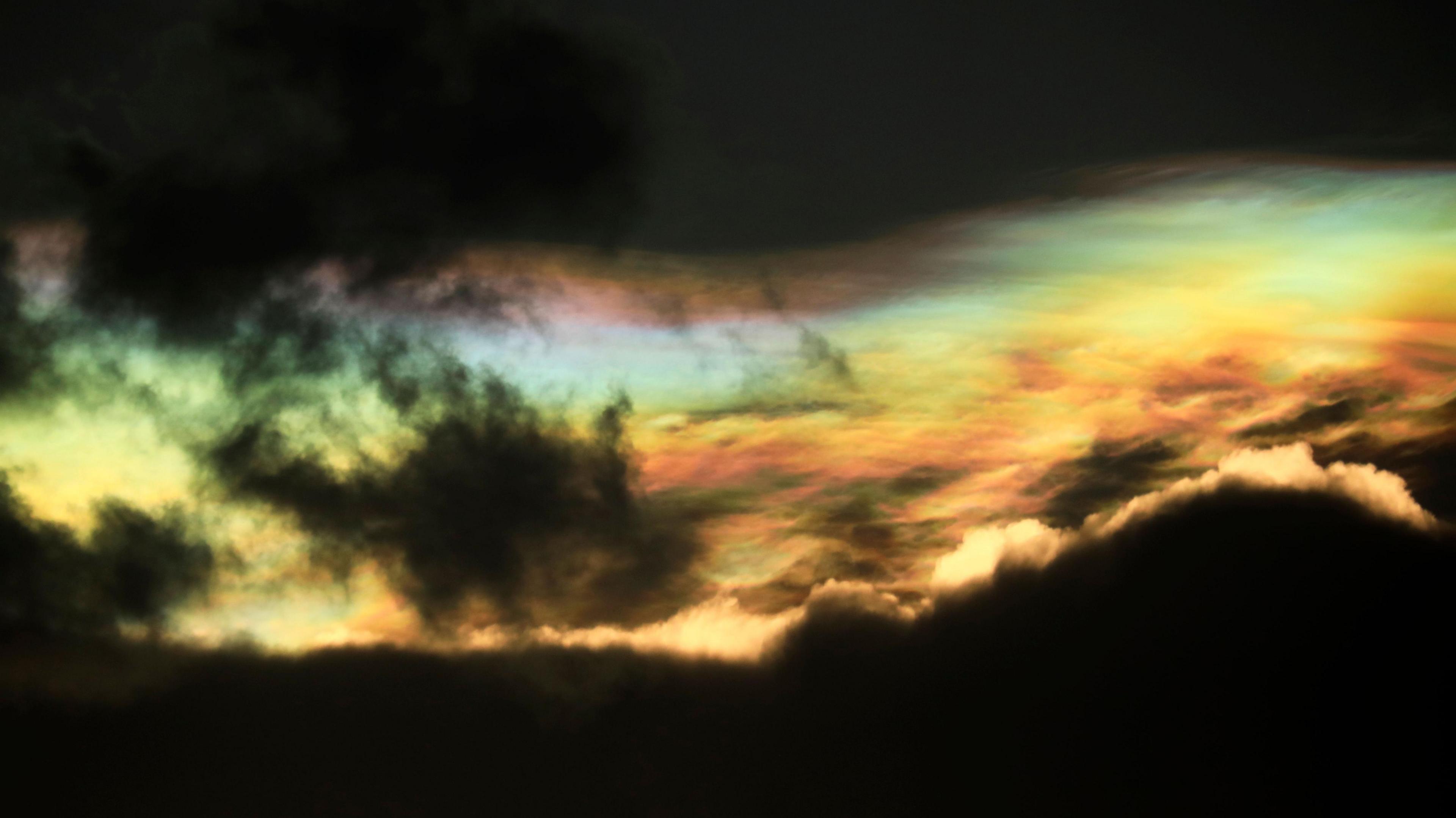 Rainbow coloured clouds can be seen through dark clouds 