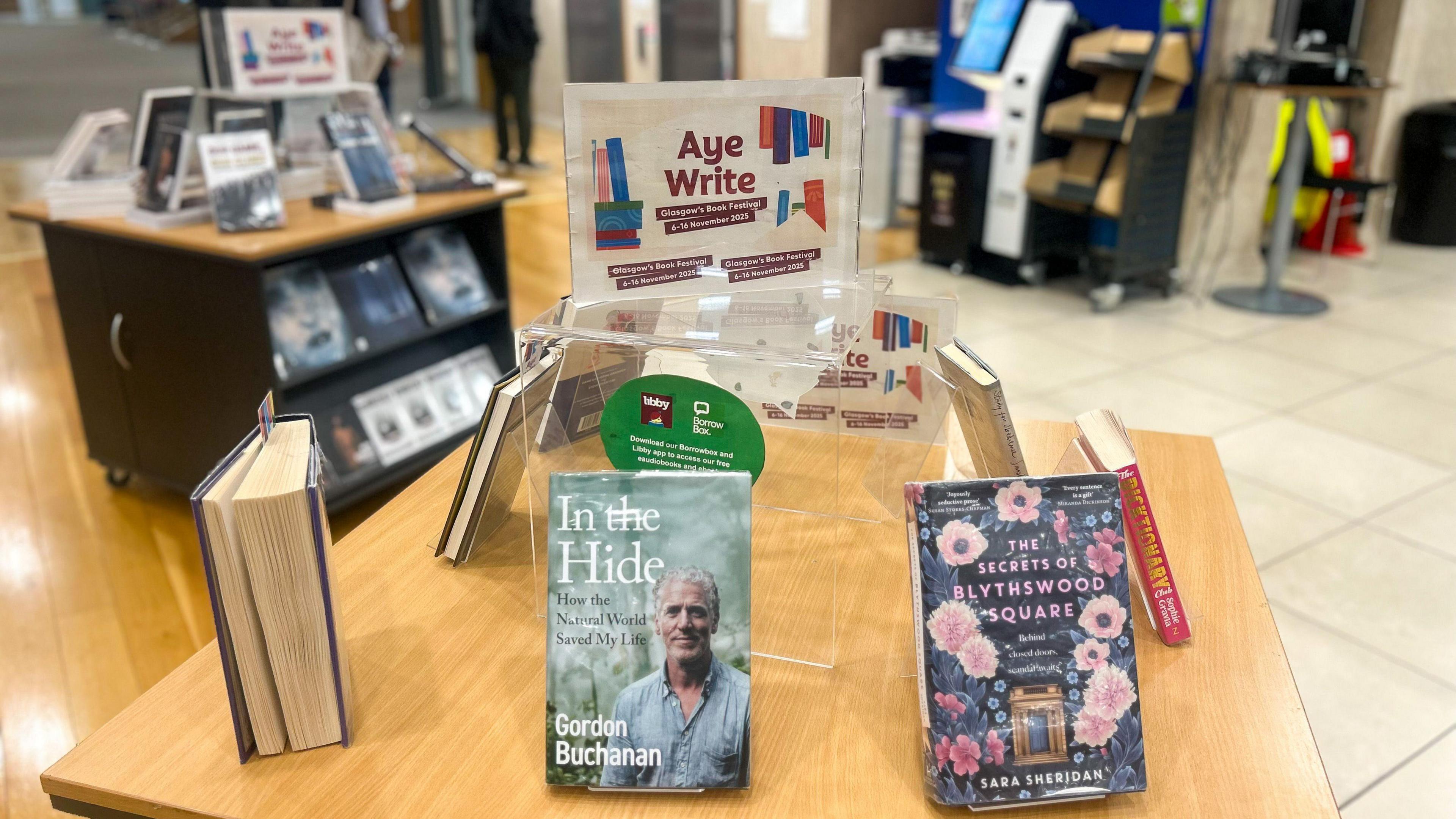 Books on a table in the Mitchell Library with an Aye Write branded sign above them.