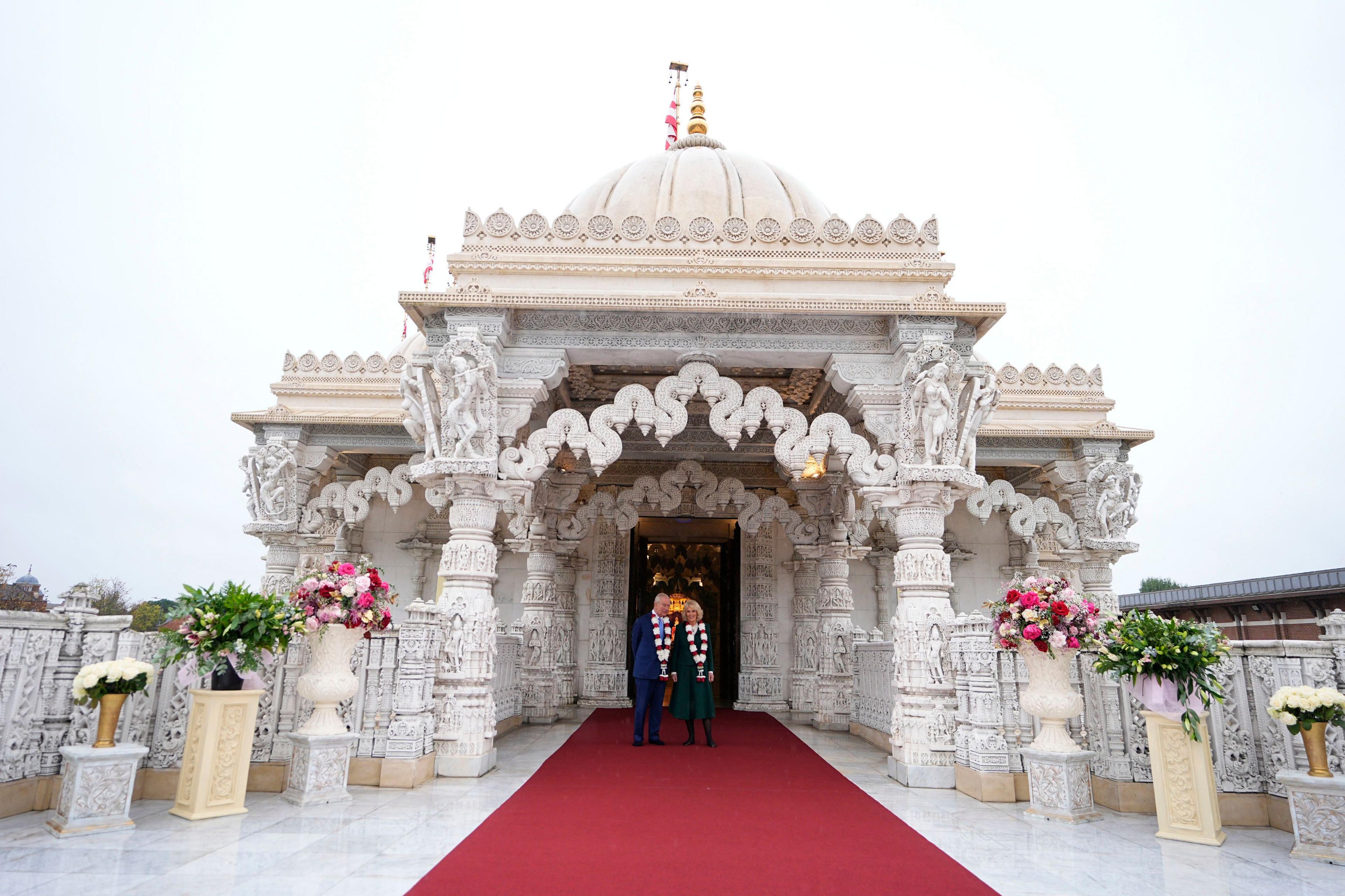 The royal couple can just be seen standing in front of an intricately carved white marble temple with vases of flowers on stands on either side.