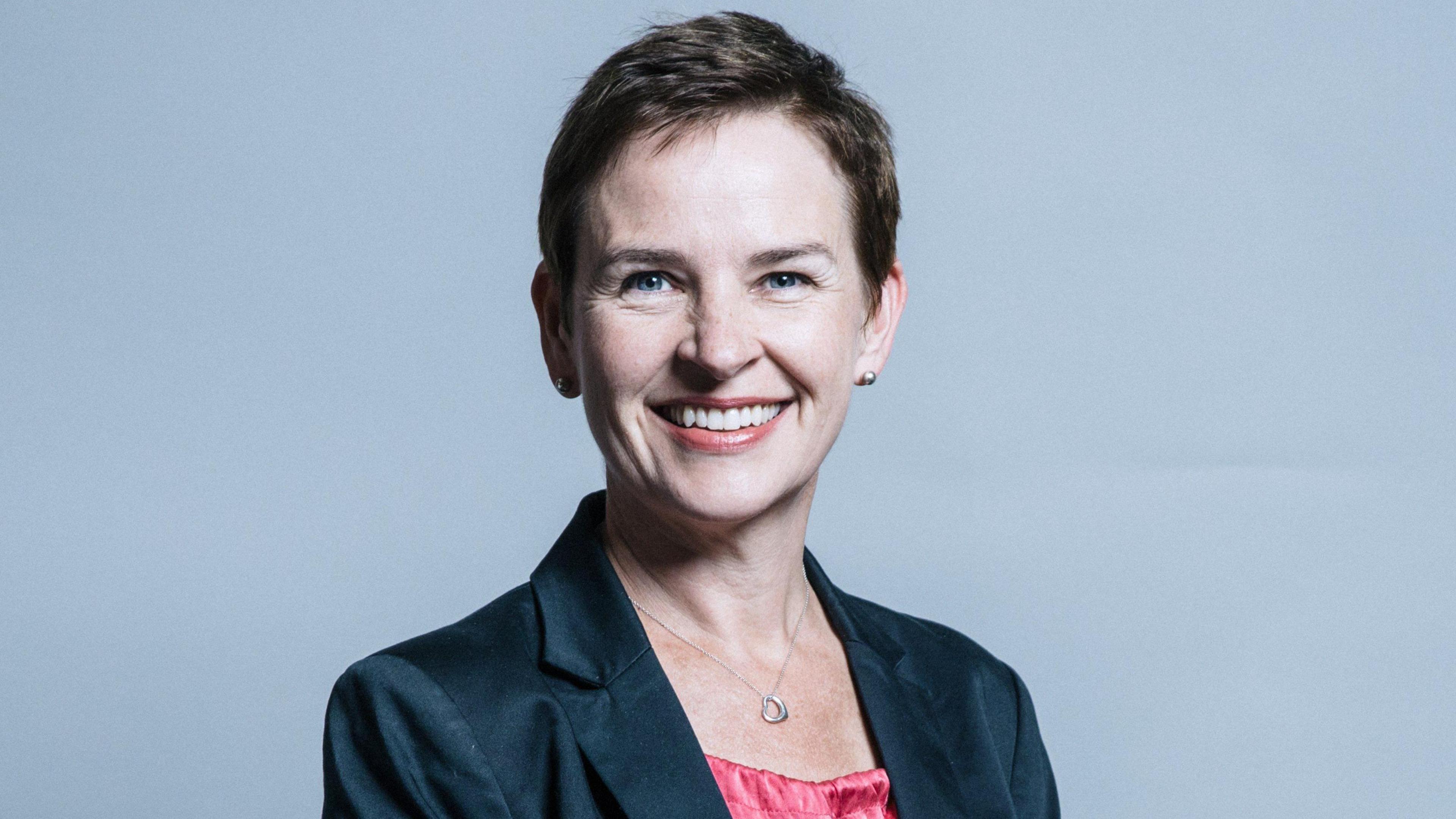 A House of Commons portrait of Mary Creagh - a woman with short brown hair, a necklace, a black jacket and a pink top - who is smiling at the camera.