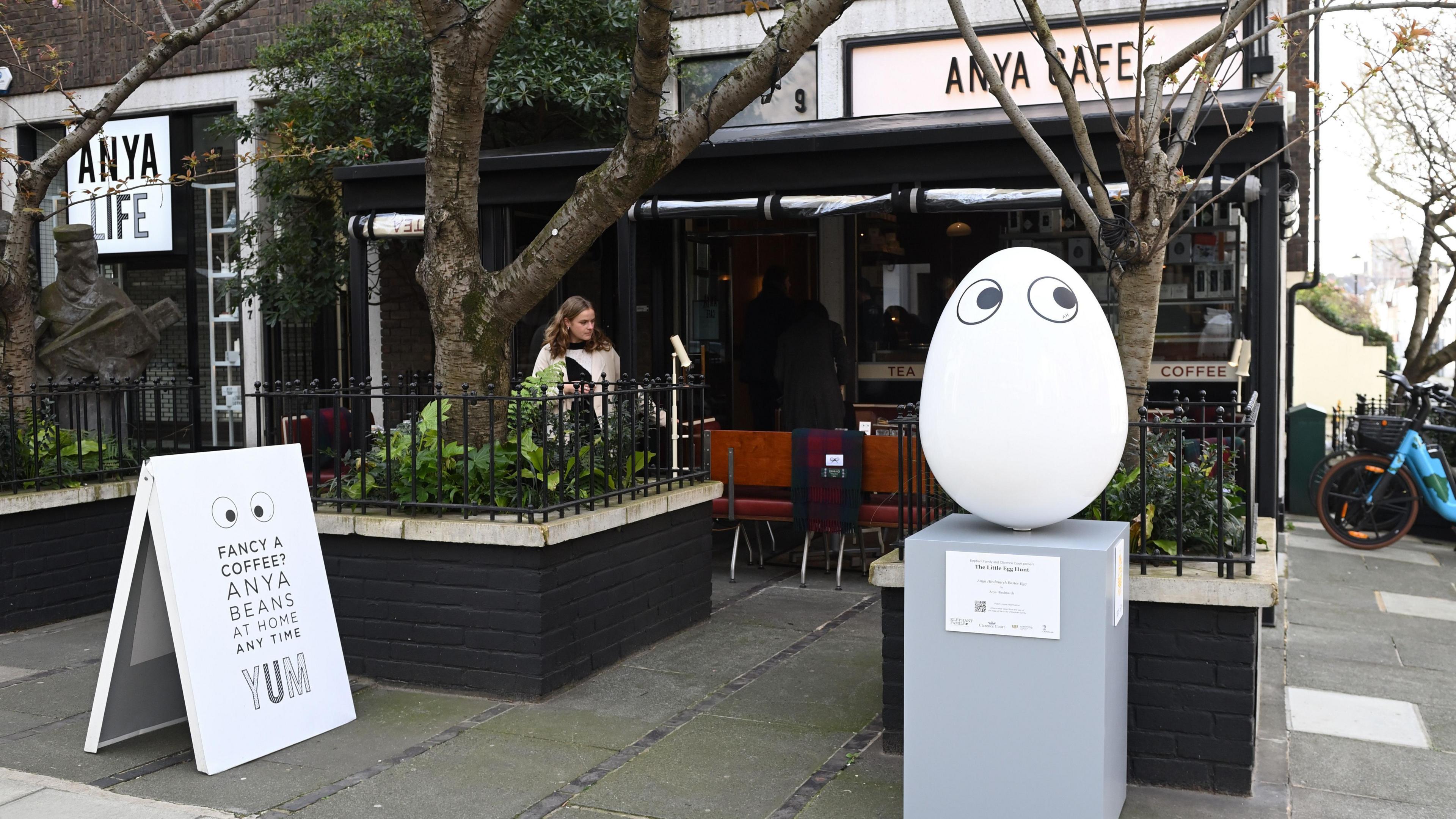 A white large egg with two eyes looking to the right in front of 'Anya Cafe'.