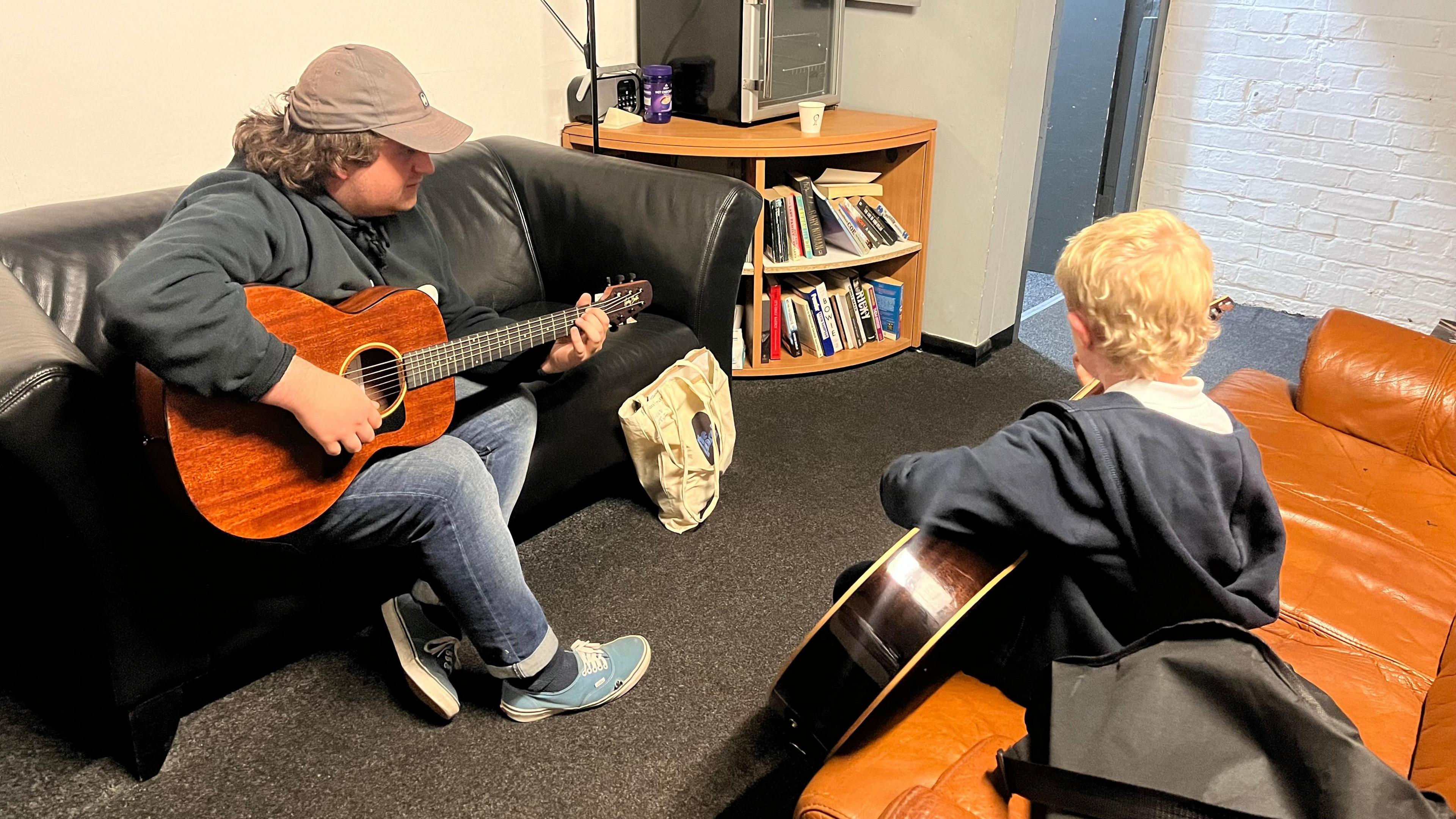 A guitar lesson being taught in the Bunker Music Studio. A tutor sits across from his student, both holding guitars.