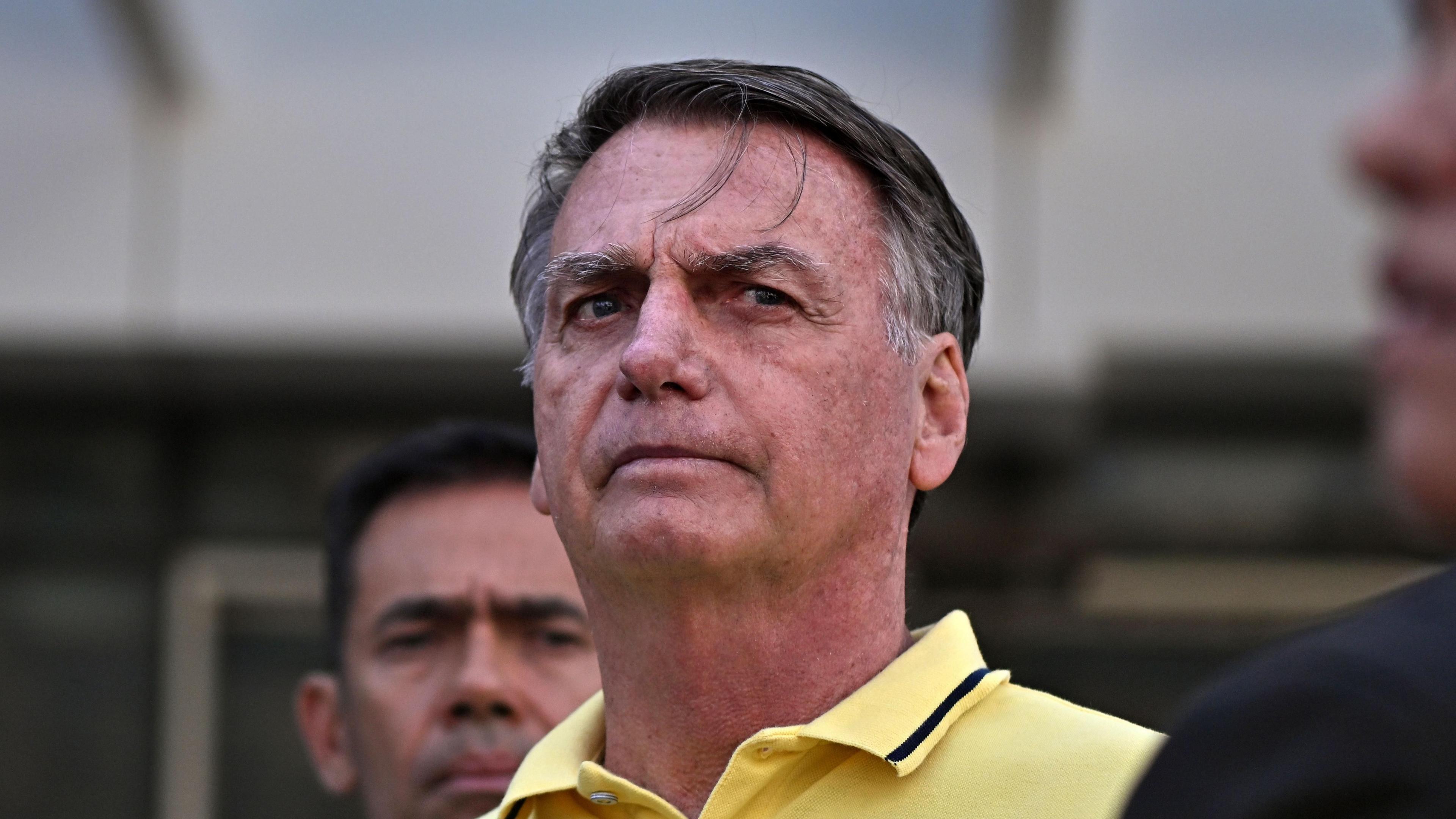 Jair Bolsonaro pictured from the neck up, in a pale yellow polo shirt with a navy trim