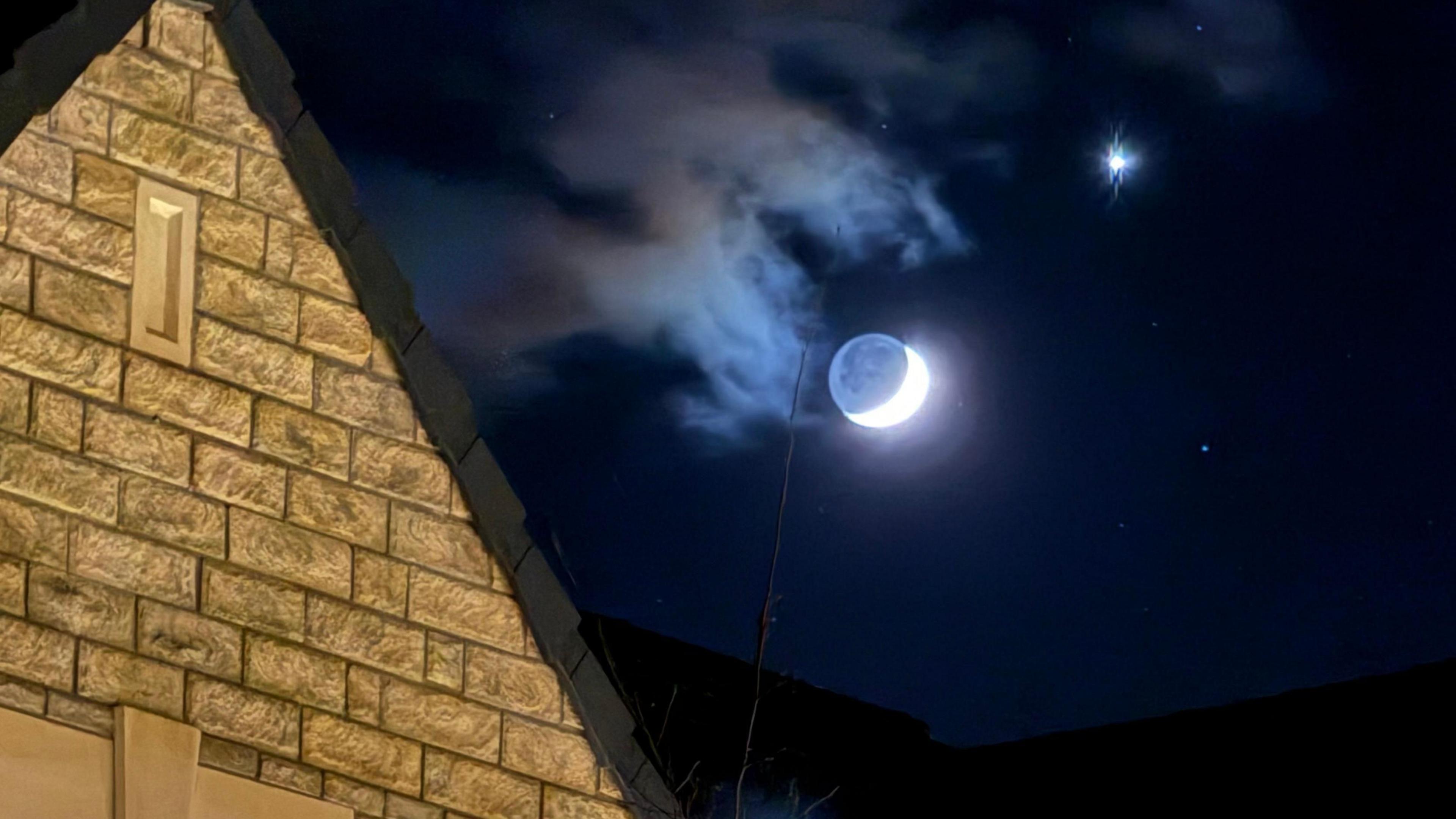 A crescent moon and Venus can be seen in the sky with a cream-brick building in the foreground.